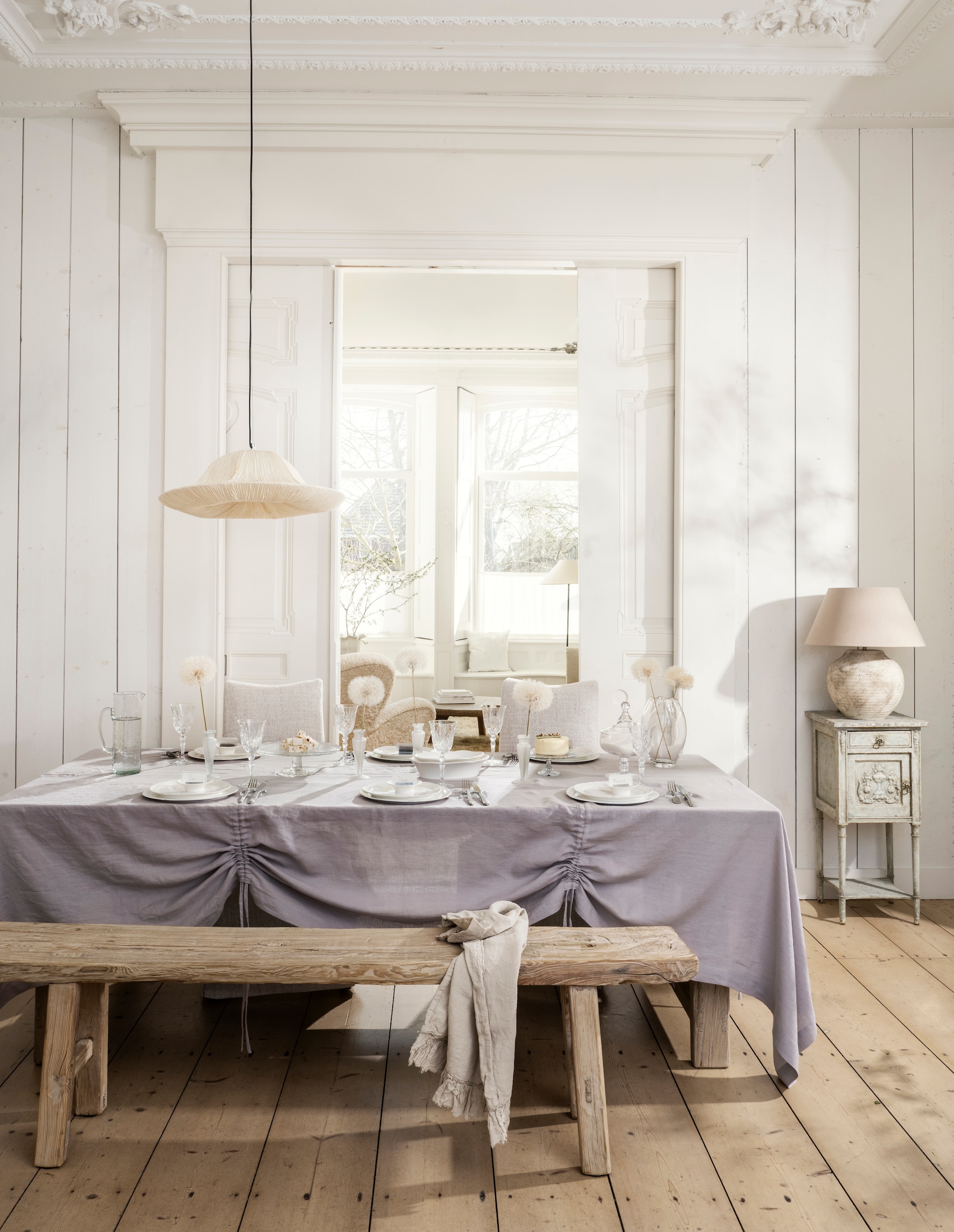 Het Kabinet Oude Chinese eettafel, iepenhout, 225x99x76 cm (lxbxh) € 2295,-, Oude Chinese bank, iepenhout, 181x27x50 cm (lxbxh) € 459,- (hetkabinet.nl). Rivièra Maison eetkamerstoelen Monti, katoen, viscose, linnen en rubberhout, antique white, 50x67x100 cm (bxdxh) € 349,- (cejorwonen.nl). Zara Home tafellamp, aardewerk, bruin € 179,-, vaas met geschulpte rand, glas € 29,99, gegraveerde wijnglazen, kristallook € 7,99, vierdelige bestekset, staal € 35,99, Colin King kandelaar (als vaas), matglas € 29,99, naamkaarthouders en kaartjes, metaal en papier, set van 8 houders en 24 kaartjes € 15,99 (zarahome.com). By-boo hanglamp Lokta 2, handgeschept papier, wit, 62,5x19,5 cm (Øxh) € 189,- (by-boo.com). Piet Jonker antiek Frans nachtkastje, hout, grijs patina, 38,5x38x83 cm (lxbxh), prijs op aanvraag (pietjonker.nl). Urban Nature Culture schenkkan, gehamerd glas € 39,99 (shop.vtwonen.nl). Taartschalen, glas (kringloop). Oury Home tafelkleed met trekkoordplooien, linnen, lila, 320x200 cm (lxb) € 325,- (ouryhome.com). Serax serviesgoed, collectie Silhouette Dinnerware, porselein, wit, vanaf € 5,-, bonbonnière, collectie The Josephine, glas € 95,- (serax.com). Kims Home Luxury geprepareerde paardenbloemen € 18,95 (kimshomeluxury.nl). vtwonen Landelijk 06-2026 | styling Kim van Rossenberg | fotografie Stan Koolen