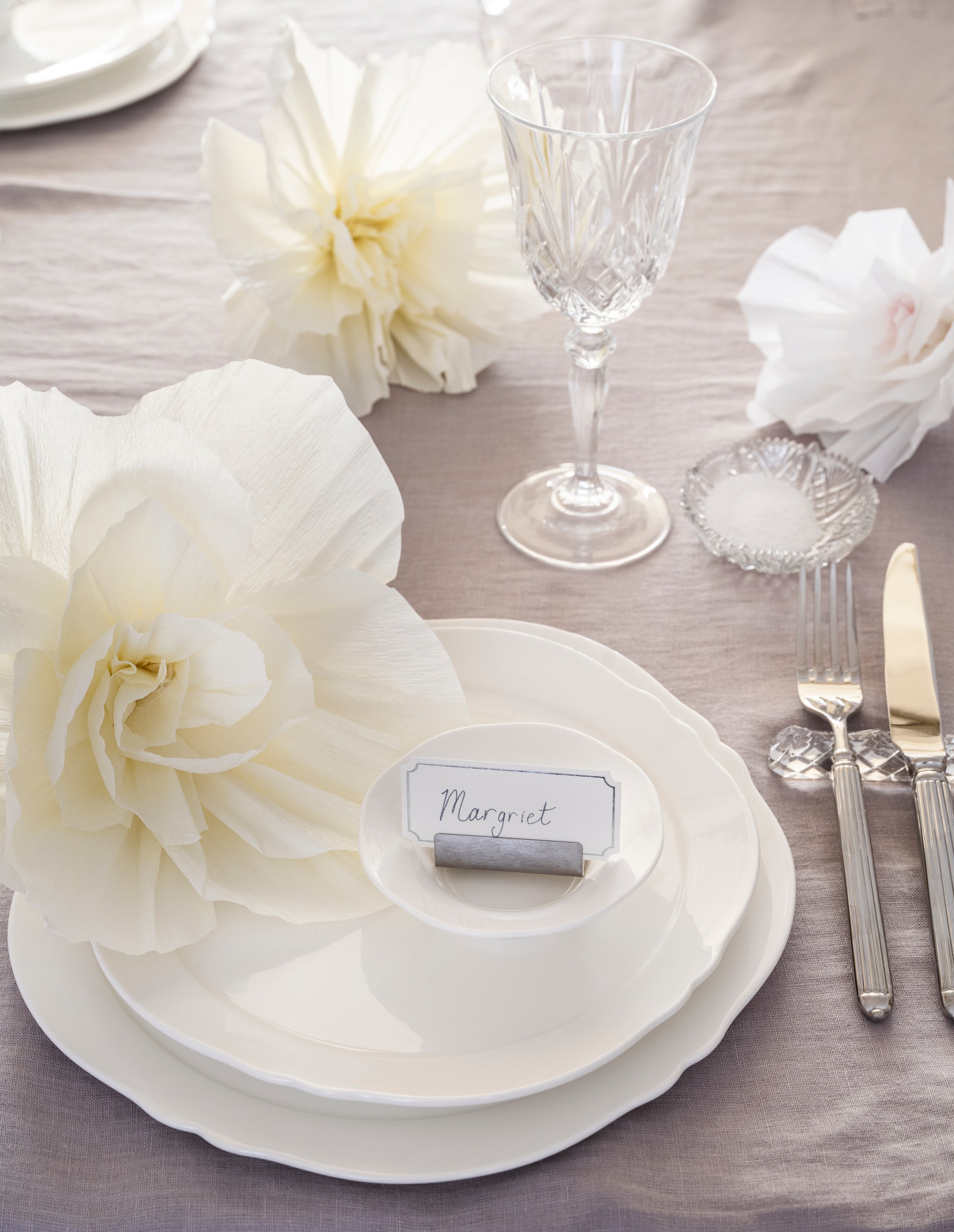 Zara Home gegraveerde wijnglazen, kristallook € 7,99, vier-delige bestekset, staal € 35,99, kandelaar Colin King (als vaas), matglas € 29,99, naamkaarthouders en kaartjes, metaal en papier, set van 8 houders en 24 kaartjes € 15,99 (zarahome.com). Urban Nature Culture schenkkan, gehamerd glas € 39,99 (shop.vtwonen.nl). Taartschaal en kleine schaaltjes, glas (kringloop). Oury Home handgemaakt tafelkleed, linnen, lila, 320x200 cm (lxb) € 325,- (ouryhome.com). Serax serviesgoed, collectie Silhouette Dinnerware, porselein, wit vanaf € 5,- (serax.com). Slinger Shop decoratiebloemen, papier, pretty powder, set van 3 € 8,99 (slingershop.nl). Schaaltje, glas (kringloopwinkel). vtwonen Landelijk 06-2026 | styling Kim van Rossenberg | fotografie Stan Koolen