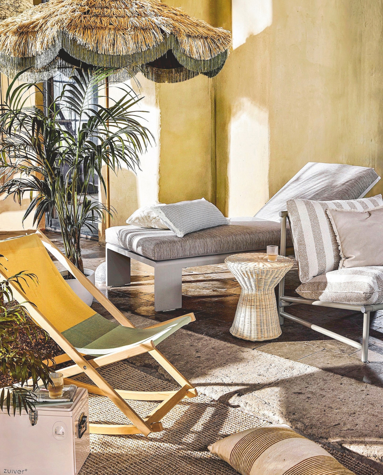 Weltevree schommelstoel Beach Rocker, beukenhout en katoen, 44x45x39 cm (bxdxh) € 239,- (weltevree.eu). HKliving parasol Serengeti, polyester, 230 cm (Ø)€ 439,- (hklving.com). Life Outdoor Living ligbed Muro, staal en soltex stof, beige frame en kussens, vanaf € 799,- (lifeoutdoorliving.com). Woood fauteuil Elvo, aluminium en outdoorstof, wit/zand € 249,- (woood.nl). Household Hardware bijzettafel Tamtam, rotan, naturel € 369,-, kussen met smalle streep, wol, wasabigroen € 95,- (householdhardware.nl). Zuiver koelbox Cooler Be Cute, metaal, cream € 79,- (zuiver.com). Intratuin vloerkleed Miyanna, 180x120 cm € 54,99, kussen met grafisch motief € 19,99, kussen zandkleur met rafelrand € 14,99, witte pot Oslo € 39,95 (intratuin.nl). Fermob kussen Evasion op fauteuil, all weather-stof, etna € 130,- (dacks.nl). vtwonen special 01-2026 | styling Marlies Does | fotografie Peggy Janssen