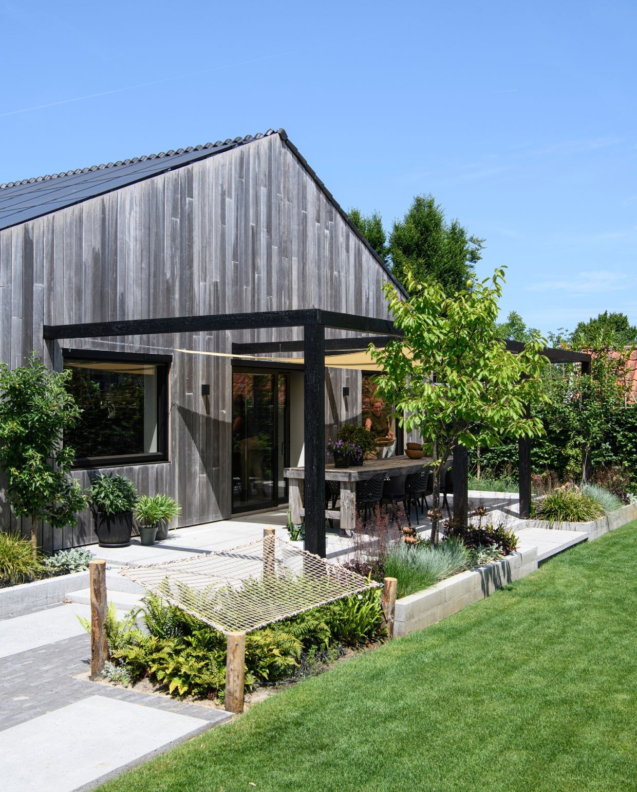 Bloempotten Intratuin. Grote tegels Schellevis. Klinkers Tumbleton ExtraCoal. Eettafel zelfgemaakt. Stoelen Kwantum. Schaduwdoek Buitenkado. vtwonen 03-2026 | styling Marit Saladini | fotografie Louis Lemaire