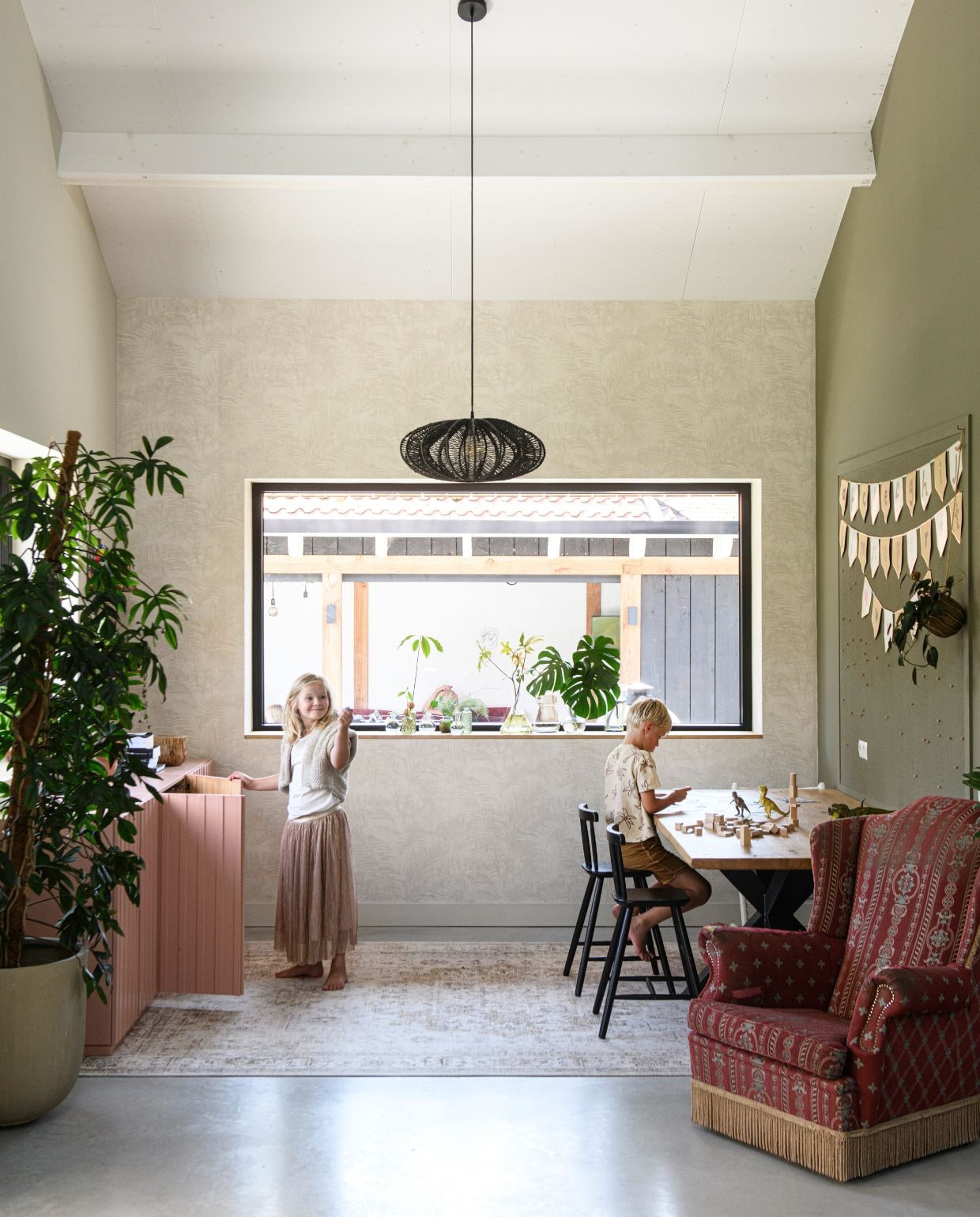 Muurverf Havermout van Gamma en Ral 7002. Behang Oasis van Eijffinger. Dressoir Ivar en eetkamerstoelen Agam van Ikea. Fauteuil erfstuk. Hanglamp Nimbus van By-Boo. Slingers Søstrene Grene. Vloerkleed Lago van Volero. Plant Intratuin. vtwonen 03-2026 | styling Marit Saladini | fotografie Louis Lemaire