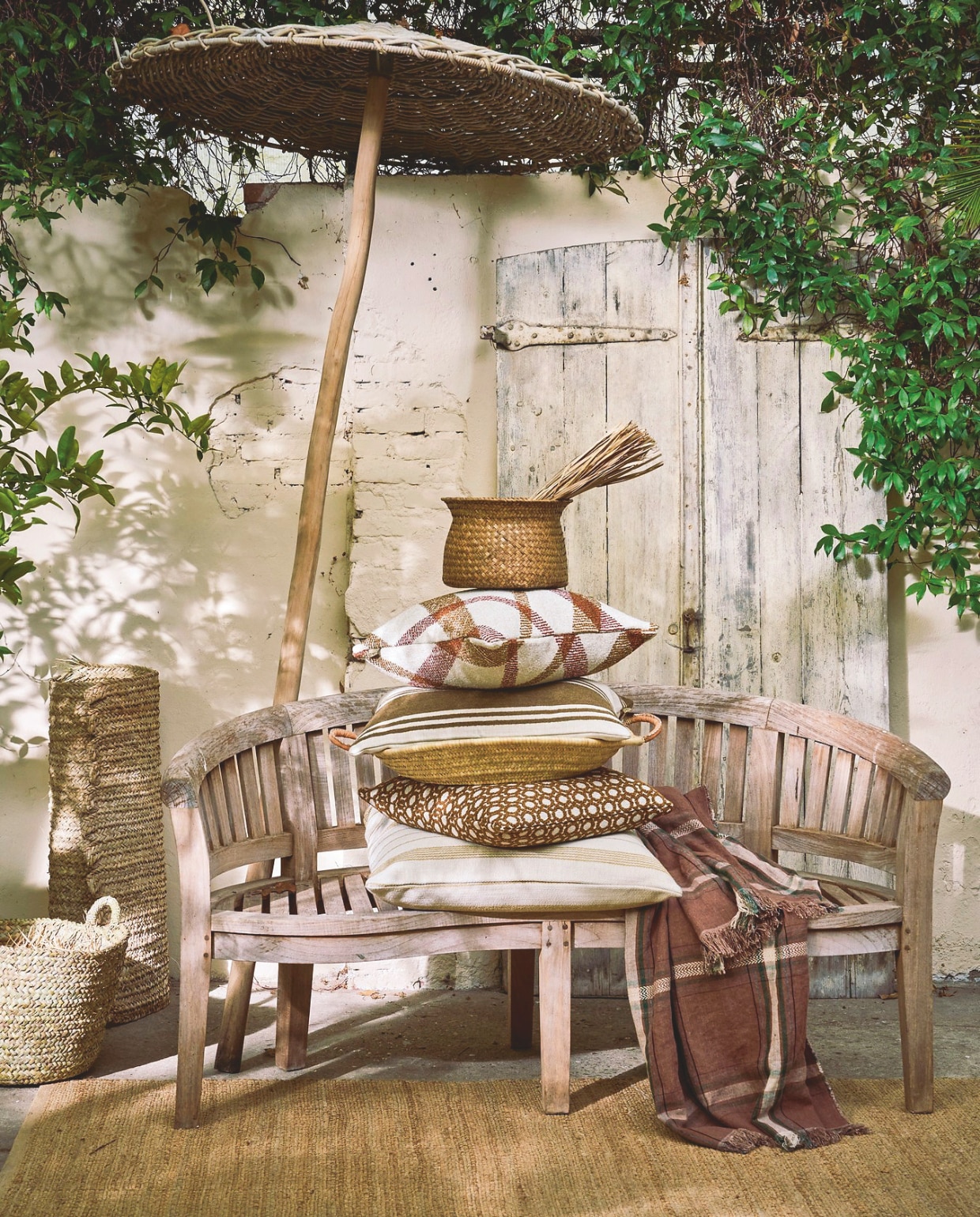 Benoa tuinbank Banana Old Style, teakhout, hout, 150x60x90 cm (bxdxh) € 399,- (meubelplaats.nl), soortgelijke parasol Heza, Spaanse heide, naturel, 220x300 cm (Øxh) € 325,- (dejapansetuin.nl). Omar Antwerp kussen Oxy, stof en dons, crème bruin, inclusief vulling € 195,-, kussen Odile, stof en dons, fijne ruit, bruin crème, inclusief vulling € 145,-, buitenkussen Stripes May Vary, stof en dons, breed gestreept, crème en bruin, inclusief vulling € 125,-, kussen Oman, stof en dons,geruit, crème en bruin, inclusief vulling € 165,- (omar-antwerp.be). Household Hardware opbergmand, gevlochten palmblad, naturel € 79,50, vloerkleed, gevlochten palmblad, naturel, prijs op aanvraag (householdhardware.nl). ’t Achterhuis siermand, riet, naturel, set van 3 € 48,40 (achterhuis.nl). HKliving vloerkleed, jute, naturel, 340x240 cm (lxb) € 329,- (shop.vtwonen.nl). Libeco doek Rowan piece de Lin, linnen, meerkleurig € 247,- (libecohomestores.eu).  vtwonen Landelijk 03-2026 | fotografie Jeroen van der Spek | styling Cleo Scheulderman