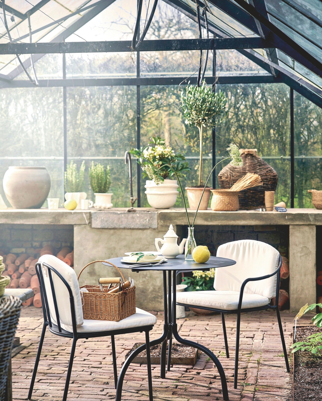 Piet Boon stoel Patio, aluminium, zwart, 54x50x76 cm (bxdxh) € 370,-, stoel Patio, met armleuningen, aluminium, zwart, 54x59x76 cm (bxdxh) € 390,-, zit- en rugkussen Patio, sneldrogend schuim en dacron, wit, 48x82x3,5 cm (bxdxh) € 100,-, bistrotafel Patio, metaal, zwart, 75x75x73 cm (lxbxh) € 395,-, pot Earth, papier-maché, wit € 185,-, pot Molly 02, keramiek, beige € 99,-, pot Molly 05, keramiek, beige € 99,-, borden Silhouette, ontworpen door Sergio Herman, porselein, wit, vanaf € 8,50 (serax.com). ’t Achterhuis pot, aardewerk, grijs € 133,10, vaas, riet, naturel € 180,-, siermand, riet, naturel, set van 3 € 48,40, vegert, riet € 9,68 (achterhuis.nl). By Mölle bestek Brick Lane, roestvrij staal, lepel € 7,-, vork € 7,-, mes € 12,- (bymolle.com). Household Hardware theepot € 49,- (householdhardware.nl). Zara Home mand, riet, bruin € 25,99 (zarahome.com). Soortgelijke kas (tuinkasgemak.nl of tuinkassenwinkel.nl). Overig privébezit. vtwonen Landelijk 03-2026 | fotografie Jeroen van der Spek | styling Cleo Scheulderman