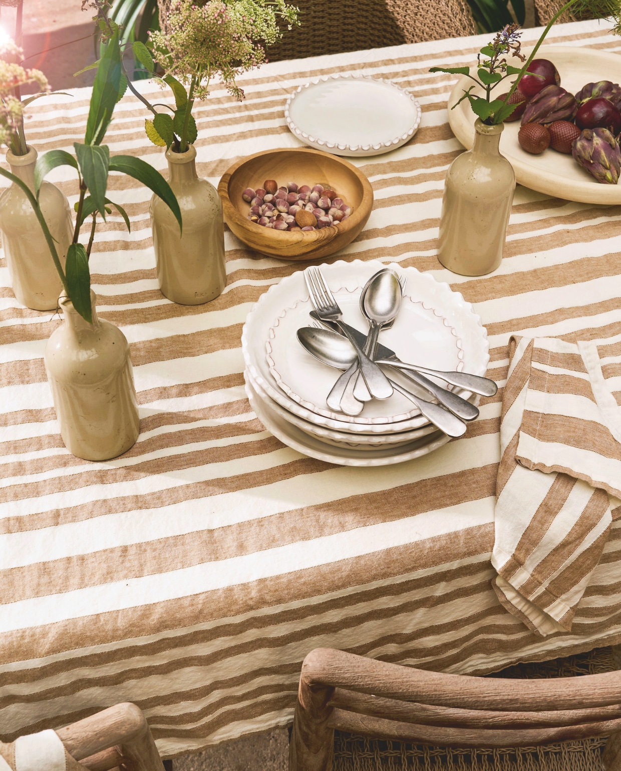 Gommaire eettafel Goss-Nac, teakhout, 250x100x76 cm (lxbxh) € 3224,-,eetkamerstoel Jared, teakhout 46x47x78 cm (bxdxh) € 444,- (achterhuis.nl). Household Hardware borden Zigzag, keramiek, naturel  € 21,- schaal, tadelakt, wit € 121,-, schaal, hout € 21,- (householdhardware.nl). Zara Home tafelkleed, linnen, bruin en wit gestreept € 69,99, servetten, linnen, bruin en wit gestreept, set van 2 € 15,99, dienblad rotan, naturel € 49,99 (zarahome.com). By Mölle bestek Brick Lane, roestvrij staal, lepel € 7,-, vork € 7,-, mes € 12,- (bymolle.com). Vazen oude kruiken en glazen limonadekruik Marktplaats. Overig privébezit. vtwonen Landelijk 03-2026 | fotografie Jeroen van der Spek | styling Cleo Scheulderman