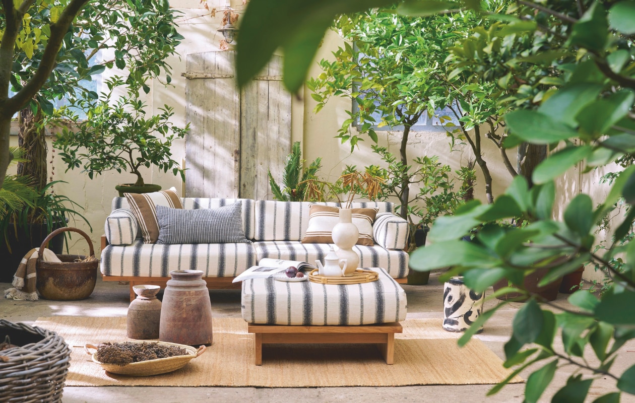 HKliving outdoorbank Chalkstripe, teak en outdoor stof, meerkleurig, 227x67x93,5 cm (bxdxh) € 3295,-, outdoor hocker Chalkstripe, teak en outdoor stof, meerkleurig, 88x88x38 cm (bxdxh) € 995,-, vloerkleed, jute, naturel, 340x240 cm (lxb) € 329,-, kussen Monochrome, zwart-wit gestreept € 54,90 (shop.vtwonen.nl). Household Hardware vaas Bubble, tadelakt, wit € 115,-, theepot, keramiek, wit € 49,-, bord, keramiek, wit € 25,-, schaal Marrakech, riet, naturel € 65,-,  (shop.vtwonen.nl). Omar Antwerp buitenkussen Olga, stof en dons, crème en bruin gestreept, inclusief vulling € 165,- en in 60x40 cm (bxh) inclusief vulling € 125,- (omar-antwerp.be). ’t Achterhuis potten, hout, bruin, vanaf € 150,-, mand, riet, naturel, vanaf € 200,- (achterhuis.nl). Serax bijzettafel 06 Sophia Pawn, ontworpen door Marie Michielsen, steengoed, zwart, 27x27x34 cm (bxdxh) € 190,- (serax.com). Libeco sierdeken Julian, linnen, gestreept € 396,- (libecohomestores.eu). Overig privébezit. vtwonen Landelijk 03-2026 | fotografie Jeroen van der Spek | styling Cleo Scheulderman