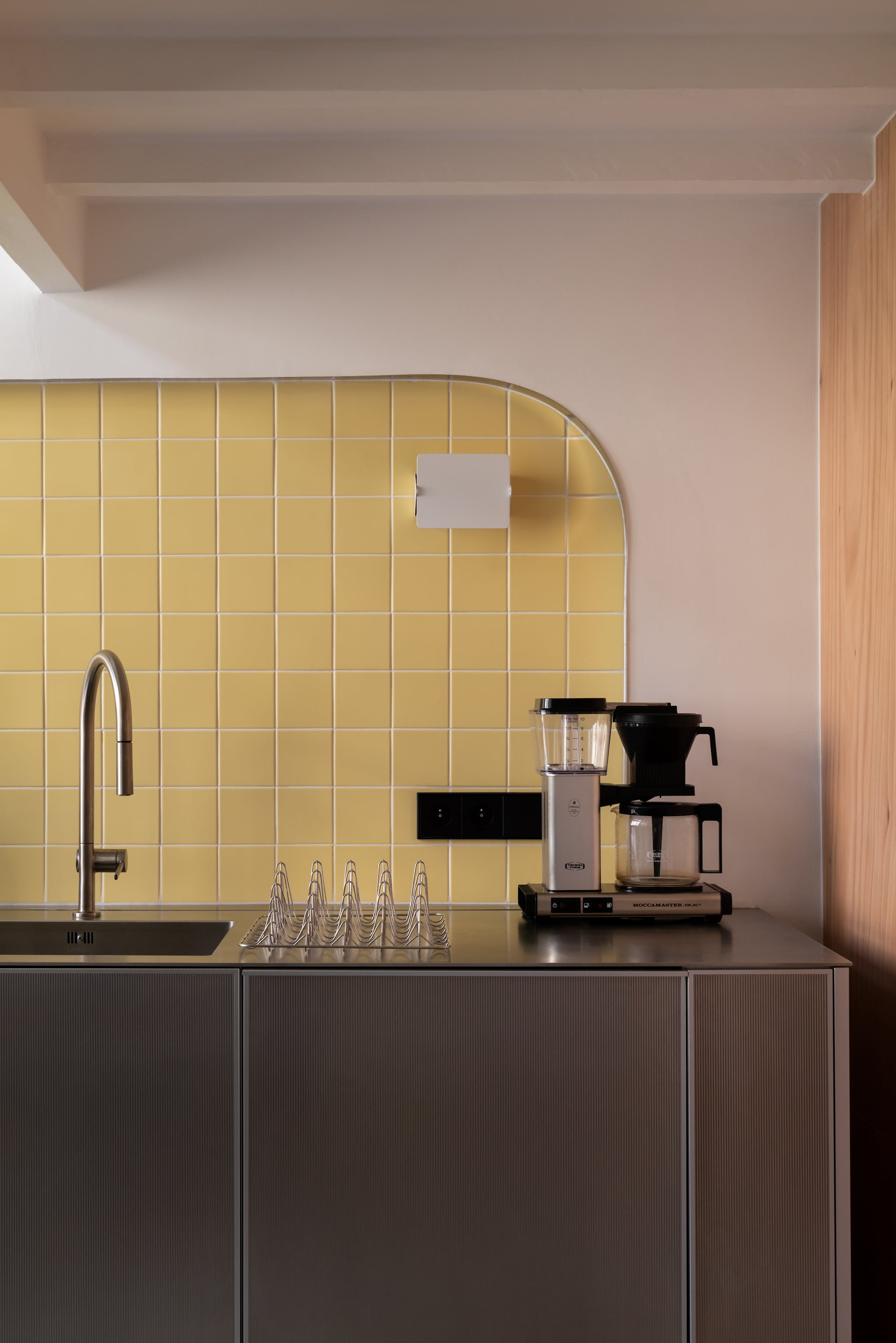 Tegels Faïence van Ce.si. Keuken Reflect door Jean Nouvel voor Reform Kitchen. Kraan Hansgrohe. Werkblad in roestvrij staal. Koffiezetapparaat Moccamaster. Wandlamp Applique à Volet Pivotant van Charlotte Perriand. vtwonen Design 06-2026 | fotografie Agathe Tissier | productie Living Agency