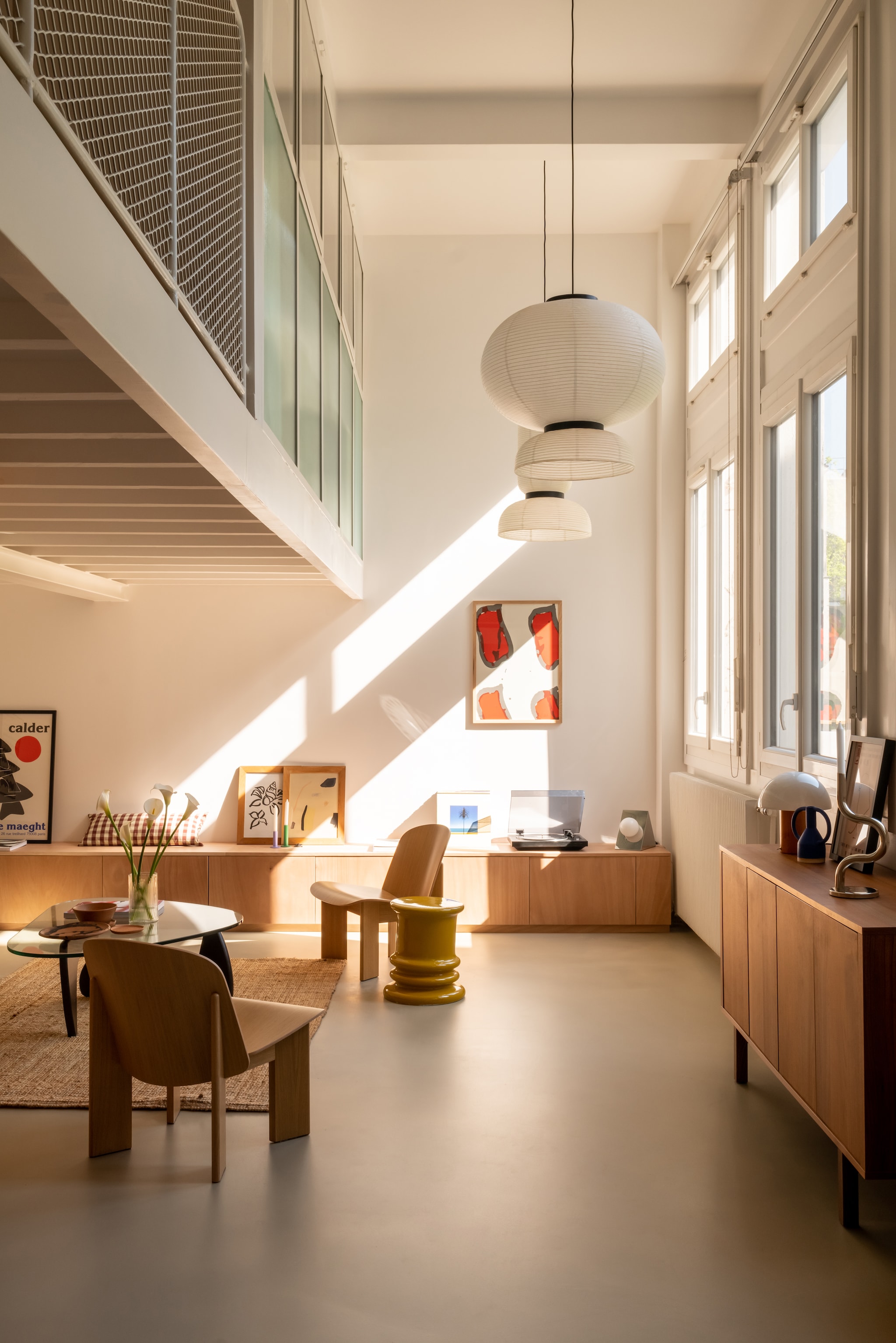 Vloer gegoten beton in kleur Borie van Mercadier. Hanglampen Formakami Jh5 en Jh3 van &Tradition. Dressoir Ikea. Bank Mags Soft van Hay, bekleed met Flamiber Olive E9 stof. Fauteuil Chisel van Hay, ontworpen door Andreas Bergsaker. Salontafel in Noguchi-stijl. Posters galerie Maeght van Alexander Calder, Shell Flower van Hôtel Magique. Zeefdruk Claude Viallat. Kruk Jean-Pierre Garrault voor Monoprix.