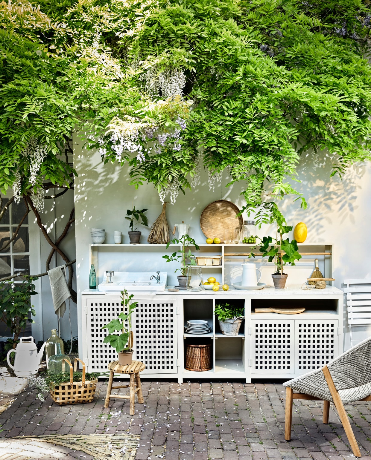 Buitenkeuken op maat gemaakt, prijs opaanvraag (com-anders). Rond bamboedienblad € 49,-, glazen kan € 33,50,glazen pot met deksel € 12,50, groteglazen flessen op de grond vanaf € 40,-(weldaad.com). Keramieken kan € 99,-,grote keramieken schaal € 129,-, wittekoffiemokken € 25,-, schaal metcitroenen € 34,- (sukha). ServiesgoedNordic Sand van Broste Copenhagen,12-delige dinner box € 133,15, wittebistro klapstoelen van Fermob € 71,-,gieter Xala Lungo € 27,70 (vtwonen.be).Linnen schort € 12,99, rotan mand inkast € 29,99 (hm.com). Buitenfauteuil€ 1810,- (dacks.nl). Bamboe kruk € 38,- (iblaursen). Koffiepot € 29,99, vegervan stro € 6,99 (zarahome.com). Grijzeterracotta bloempotten vanaf € 0,99(intratuin.be). Houten serveerplank€ 21,50 (madamstoltz.dk). Overigprivébezit. vtwonen 07-2020 | styling Cleo Scheulderman | fotografie Jeroen van der Spek