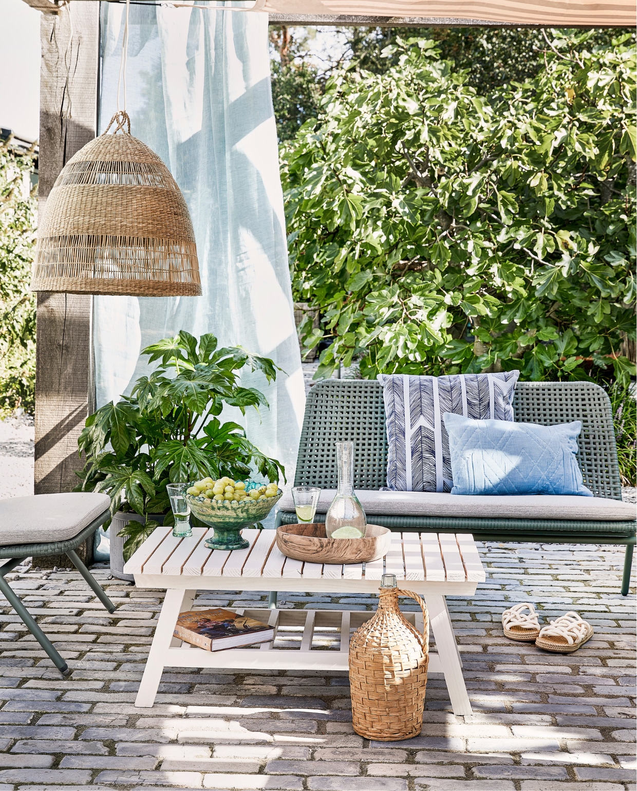 Bank Wivinia € 419,- en stoel Wivinia € 211,50 van Kave Home (vtwonen.nl). Gordijn gemaakt van linnen stof per meter € 25,- (ochreandred.nl). Kussen met print Heringbone € 25,95, lichtblauw kussen Naida € 19,99 (intratuin.nl). Schaal op voet € 99,95, walnoothouten schaal € 75,-, glazen karaf Cigogne € 23,50, glazen op voet Diabolo per stuk € 6,80 (householdhardware.nl). Instappers € 35,99 (zarahome.com). Rieten lamp Torared € 39,95 (ikea.com). Plaid Native Fan € 34,99 (sissy-boy.com). Sisal kussen € 25,- (loods5.nl). Overig privébezit. vtwonen tuin special 04-2021 | productie Corrien Flohil | uitvoering Johan Snoodijk @snoodijkenco | styling Moniek Visser | fotografie Peggy Janssen