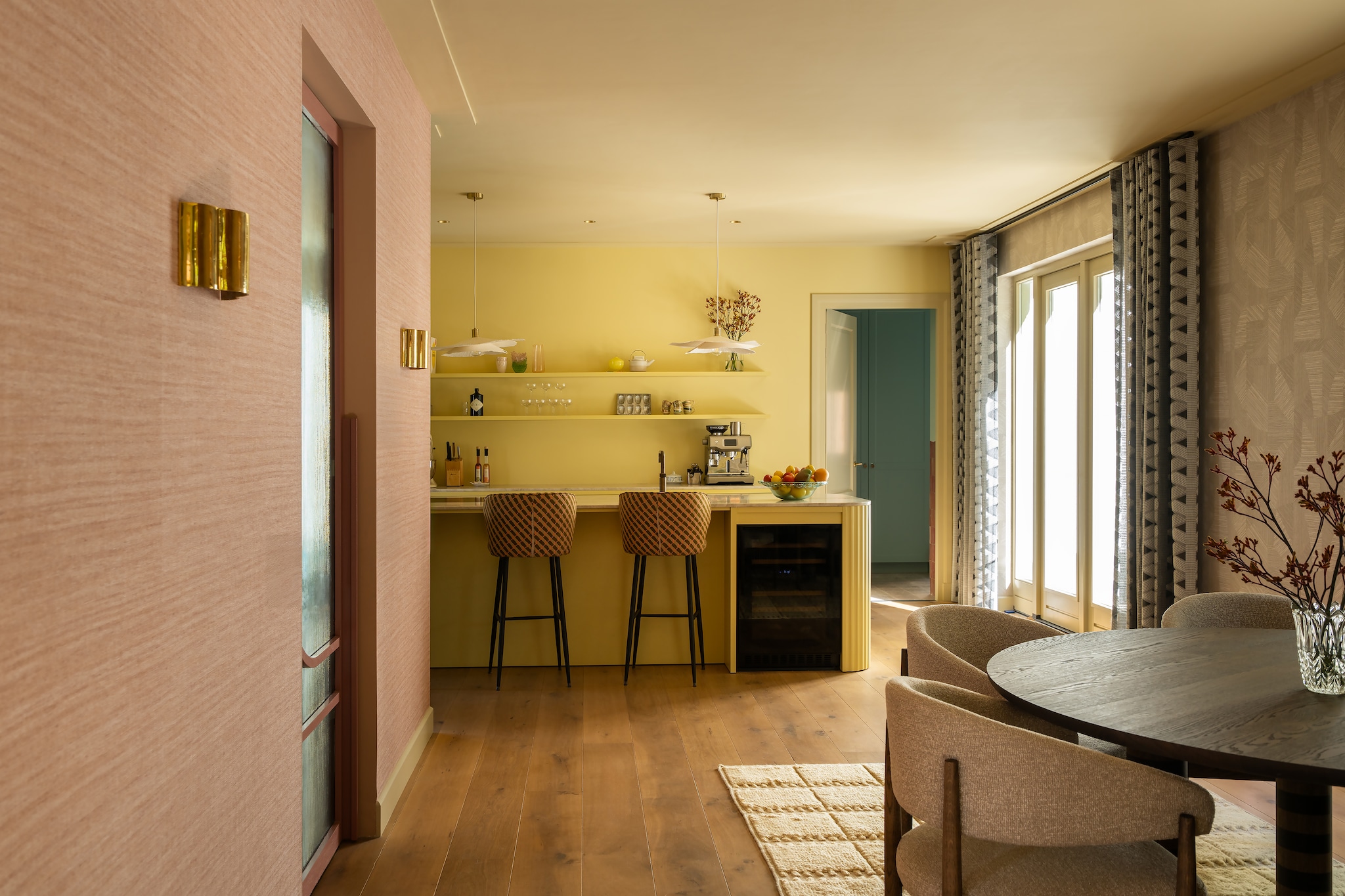 Keuken maatwerk met blad van Taj Mahal-kwartsiet. Barstoelen Kave Home, bekleed met stof 10966.56 van Nobilis. Hanglampen Zara Home. Wandlamp Sézane. Vloerkleed Layered. Gordijnen Toppoint. Verfkleur achterwand Hound Lemon, keukenblok in Gervaise Lemon, kozijnen en plafond Light Stone van Farrow & Ball. Behang Arte Lignes 40508 en Arte Essentials Tangram Caprice Linen 24004. Eetkamerset Table Du Sud. Vloer van verouderde eikenhouten planken via eikenvloerdelen.nl. Glazen deur Brouwer. vtwonen Design 06-2026 | styling Juliette de Dreu | fotografie Lotte van Uittert