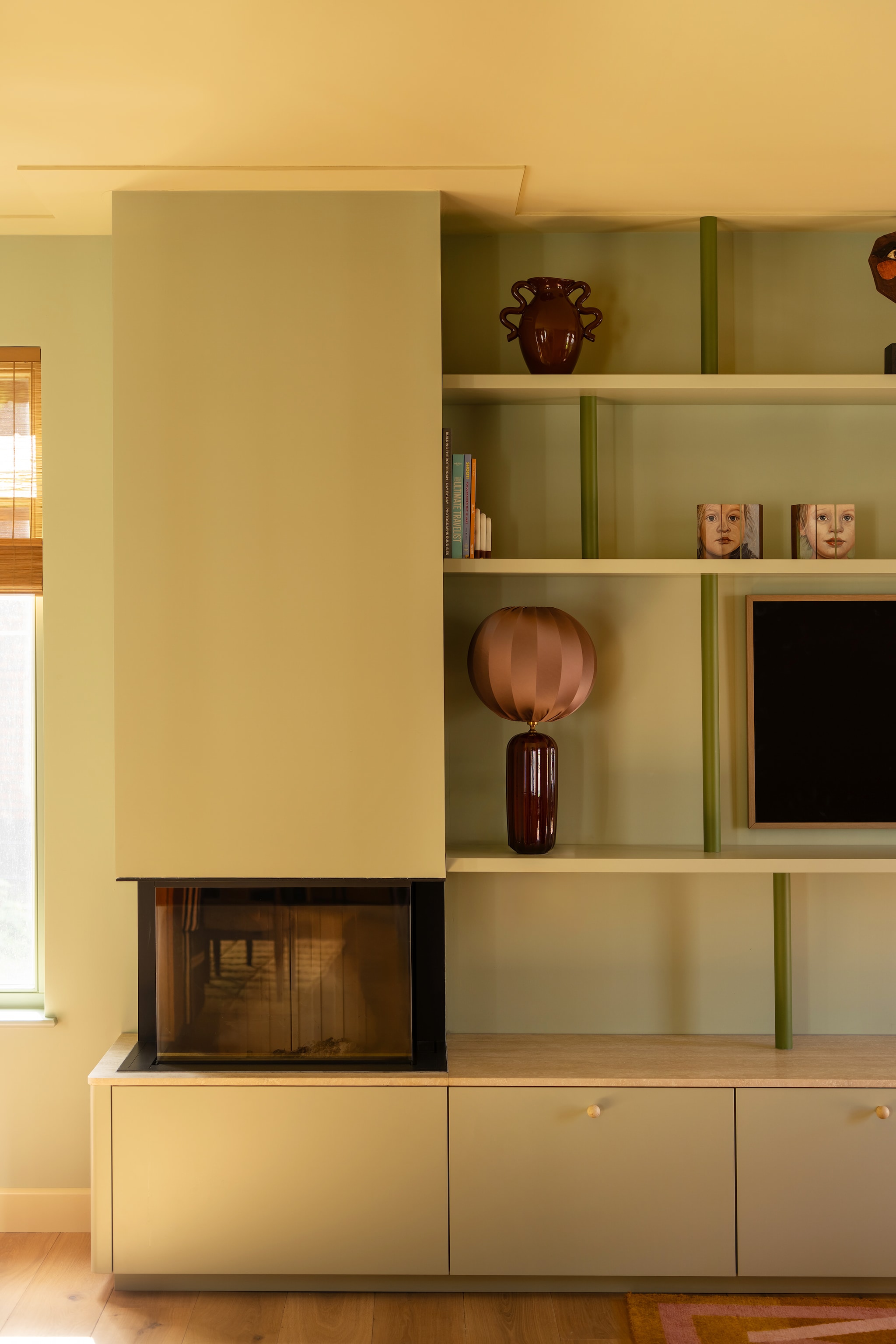 Kast maatwerk door Marijn Interieurs. Kleur Vert de Terre, spijlen in Lichen van Farrow & Ball. Knopjes via Etsy. Vaas Ferm Living. Lamp Sézane. Haard Brenzelle Premium A-3rl-80-h via Spartherm. vtwonen Design 06-2026 | styling Juliette de Dreu | fotografie Lotte van Uittert