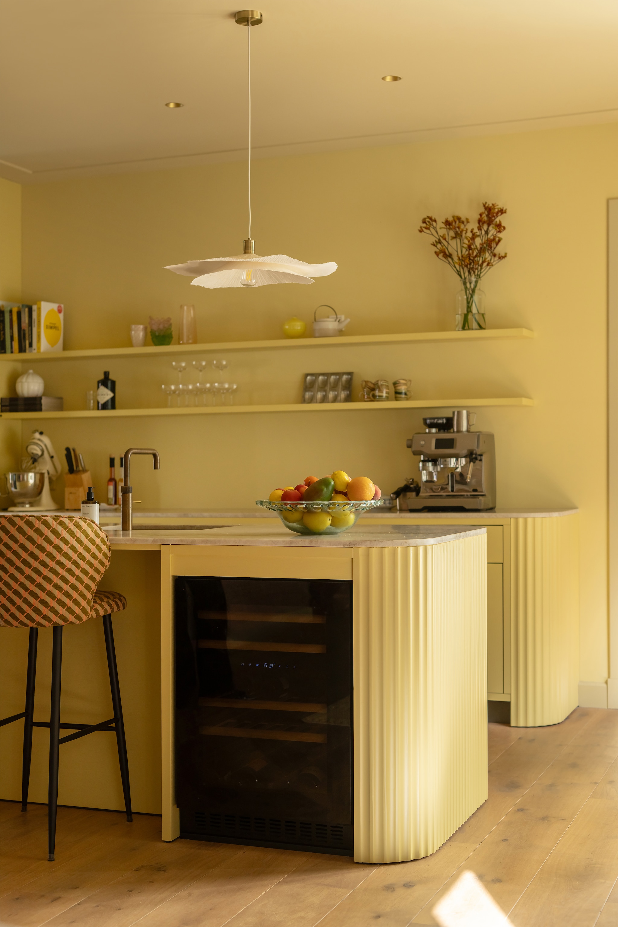 Keuken maatwerk met aanrechtblad van Taj Mahal-kwartsiet. Barstoelen Kave Home, bekleed met stof Stripes 10966.56 van Nobilis. Hanglampen Zara Home. Kleur keukenblokken Gervaise Lemon, plafond Light Stone, wand Hound Lemon van Farrow & Ball. Behang Arte Essentials Tangram Caprice Linen 24004. Wandlamp Sézane. vtwonen Design 06-2026 | styling Juliette de Dreu | fotografie Lotte van Uittert
