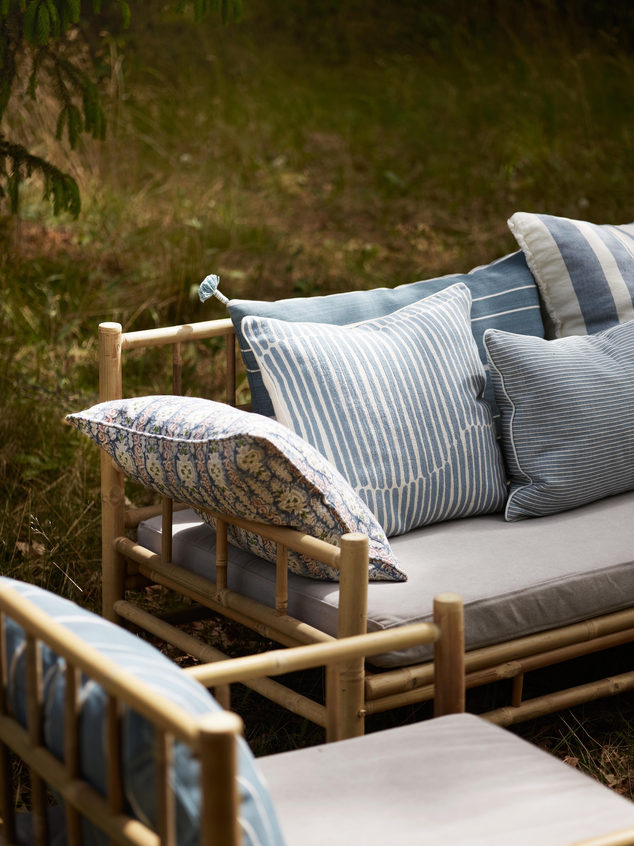 Tine K Home kussen print Agralin met Indiase blokdruktechniek, linnen, blauw € 65,82, kussen Lane, katoen, denim € 65,82, kussen Ribb, katoen, denim € 46,46, kussen Mali, katoen, denim en wit gestreept € 78,41, bank, bamboe, 177x76x70 cm (lxbxh) € 913,55 (tinekhome.com). vtwonen Landelijk 06-2026 | Tine K