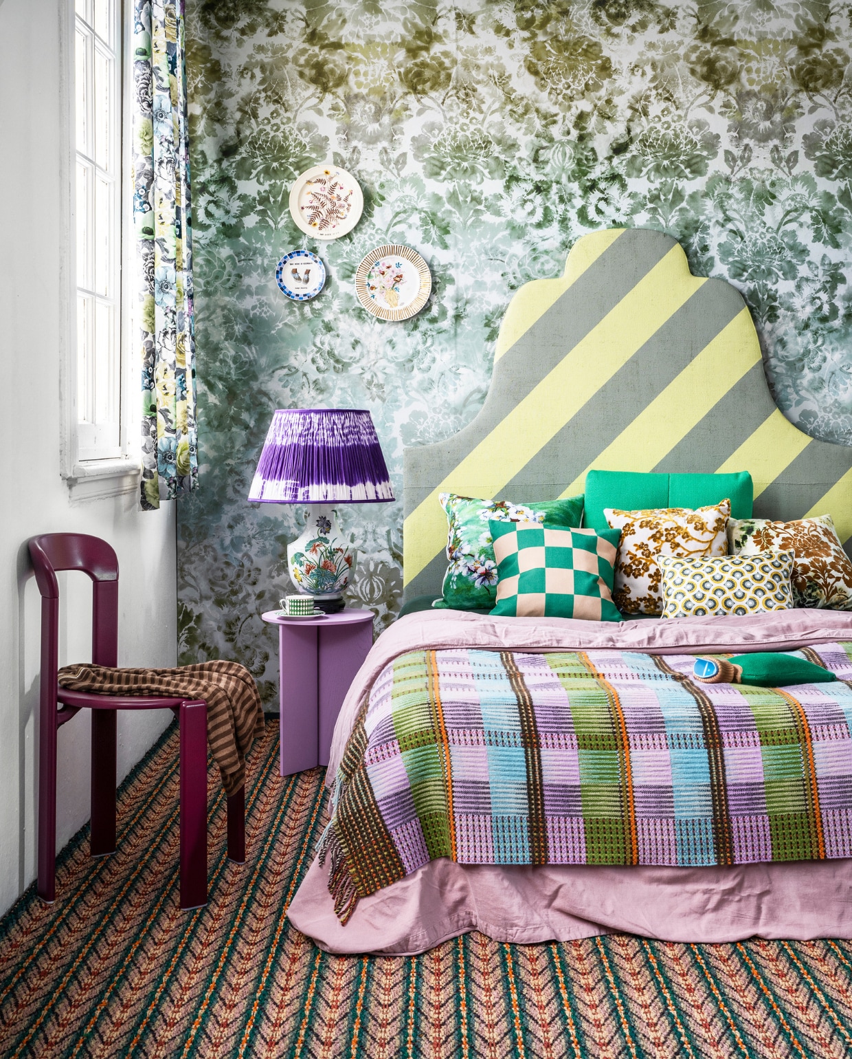 Behang Tarbana Damask van Designers Guild, 140×300 cm € 312,-, gebloemde gordijnstof Oriana van Designers Guild, 140 cm breed € 118,- (wva.nl). Gestreepte kokos vloerbedekking nr. 9022, per m2 € 97,- (cunera.nl). Bedhoofdeind van Combitex met groen-gele diagonaal geverfde strepen, prijs op aanvraag (com-anders.nl). Lila tafel van hout en staal € 215,-, stoel Rey in Grape Red € 559,-, groen rugkussen Quilton € 180,- (hay.nl). Roze linnen dekbedovertrek, 140×220 cm € 109,-, kruik € 39,95 (suite702.com). Geruite wollen plaid € 182,-, groen bloemenkussen, 60×60 cm € 174,-, bruin velours gedecoreerd kussen rechts Designers Guild € 131,- (wva.nl). Groen-naturel geruit kussen € 39,- (festamsterdam.nl). Velours kussen met Japanse bloesem van Zuiver € 40,50, kop-en-schotel van Pols Potten, per 4 € 145,- (vtwonen.nl). Vierkant zijden kussen van Lelievre € 89,- (loggerewillpower.com). Paarse tie dye lampenkap uit de Tribal collection van Vaughan Designs € 343,- (wva.nl). Gebloemde vintage lampenvoet € 85,- (hetgroteavontuur.nl). Vintage borden gedecoreerd door Lot Moorrees vanaf € 65,- (polspotten.nl). Kleding (vintagebrands.eu). vtwonen 06-2022 | styling Marianne Luning | fotografie Stan Koolen