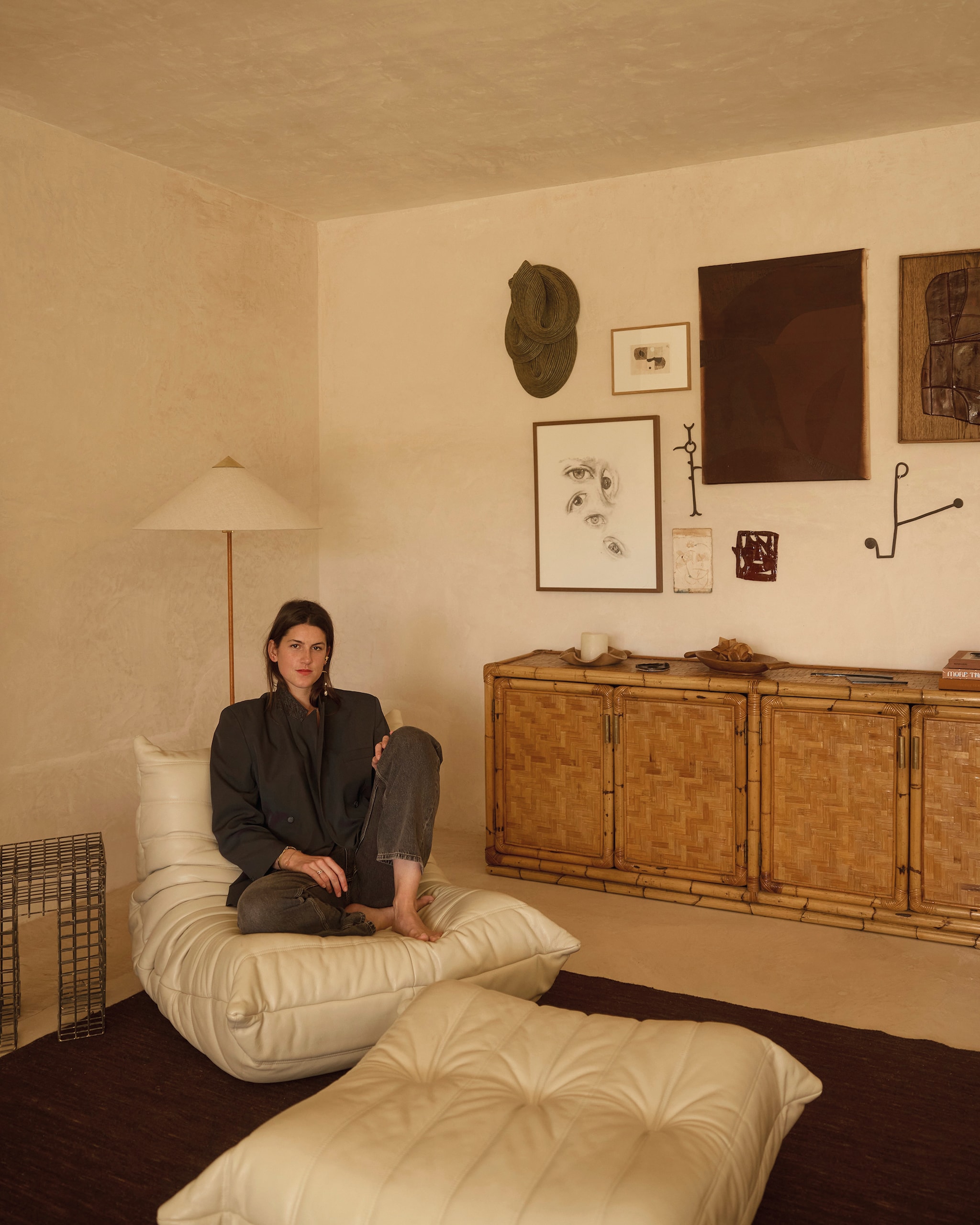 Stoel Togo van Ligne Roset. Bijzettafel en dressoir vintage. Vloerlamp 9602 van Gubi. Wandsculptuur textiel Sini Villi. Telegram letters Natalie Rich Tambien. Tekening ogen van alle kinderen in het gezin, schilderijen en keramiek eigen werk. Jurk Isabel Marant. Blazer vintage.