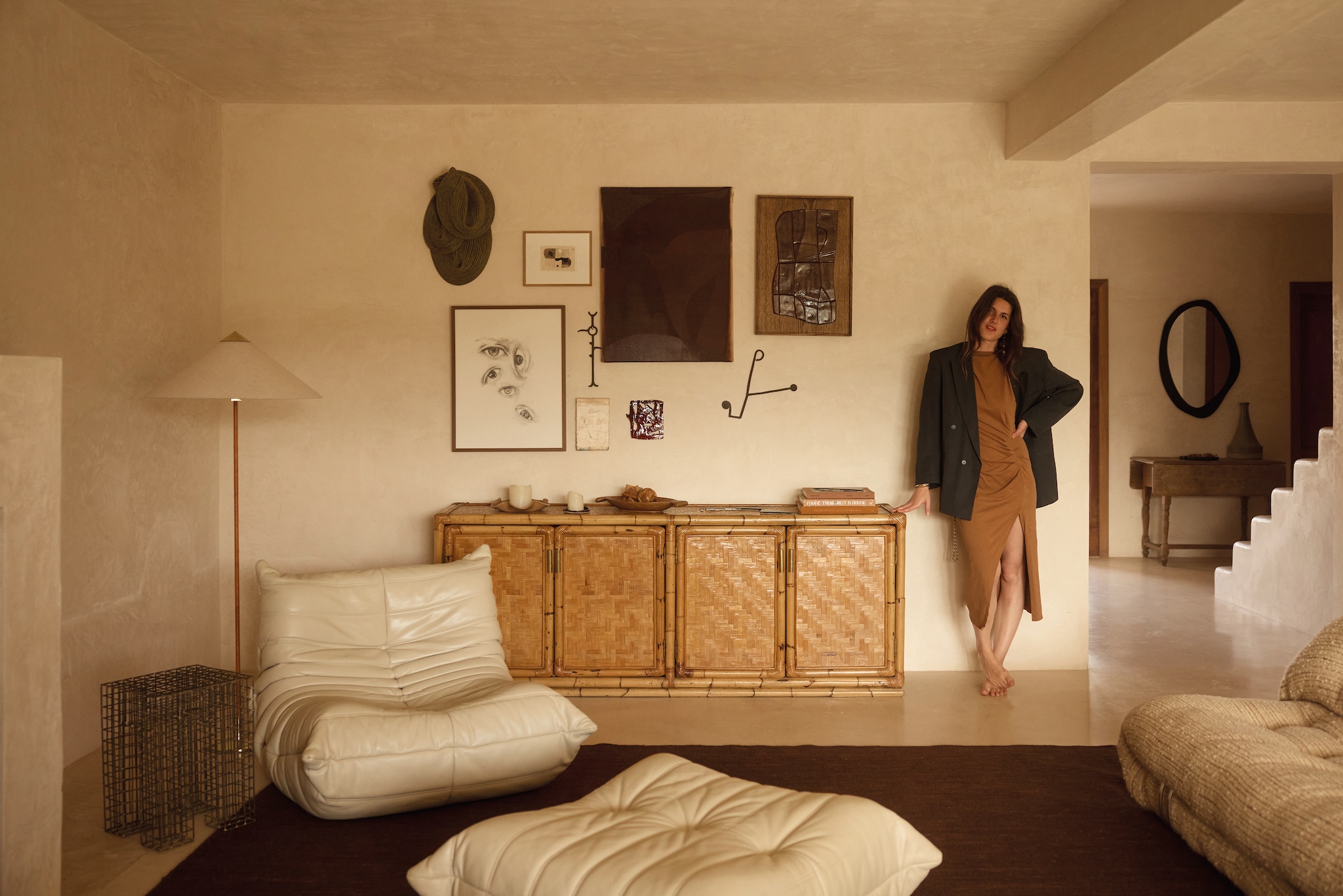 Stoel Togo van Ligne Roset. Bijzettafel en dressoir vintage. Vloerlamp 9602 van Gubi. Wandsculptuur textiel Sini Villi. Telegram letters Natalie Rich Tambien. Tekening ogen van alle kinderen in het gezin, schilderijen en keramiek eigen werk. Jurk Isabel Marant. Blazer vintage. vtwonen design 03-2026 | fotografie Daniëlle Siobhán