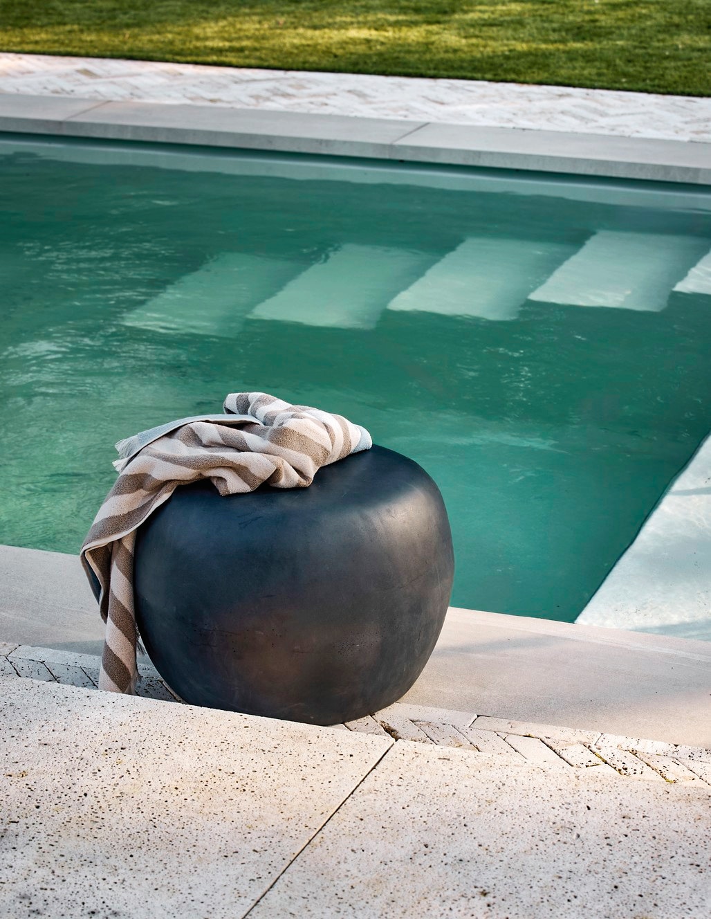 vtwonen hocker/bijzettafel Relax, fsc-gecertificeerd acaciahout en stof, naturel en zand, 90x60x40 cm (bxdxh) € 349,-, vtwonen bijzettafel Pebble, betonlook fiberclay, antraciet, 50x35 cm (Øxh) per stuk € 199,-.M.m.v. zarahome.com (plaid), loods5.nl (schaal, handdoek). Overig privébezit. vtwonen 04-2026 | styling Kim van Rossenberg | fotografie Peggy Janssen