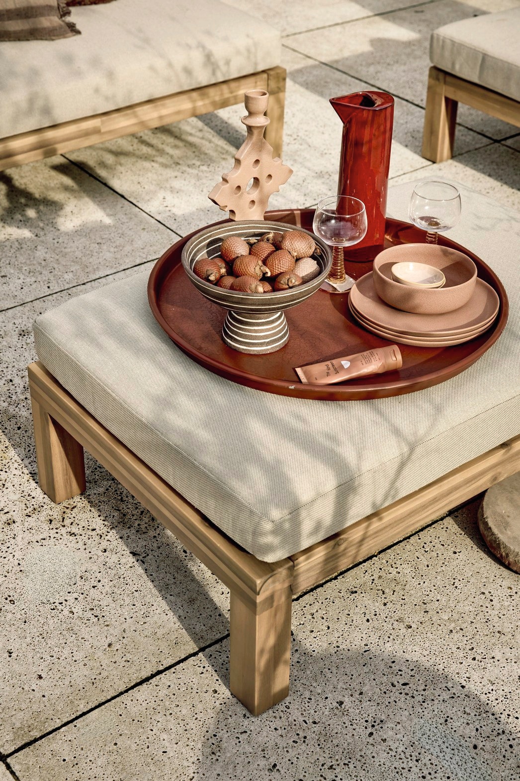 vtwonen hocker/bijzettafel Relax, fsc-gecertificeerd acaciahout en stof, naturel en zand, 90x60x40 cm (bxdxh) € 349,-, vtwonen bijzettafel Pebble, betonlook fiberclay, antraciet, 50x35 cm (Øxh) per stuk € 199,-.M.m.v. zarahome.com (plaid), loods5.nl (schaal, handdoek). Overig privébezit. vtwonen 04-2026 | styling Kim van Rossenberg | fotografie Peggy Janssen