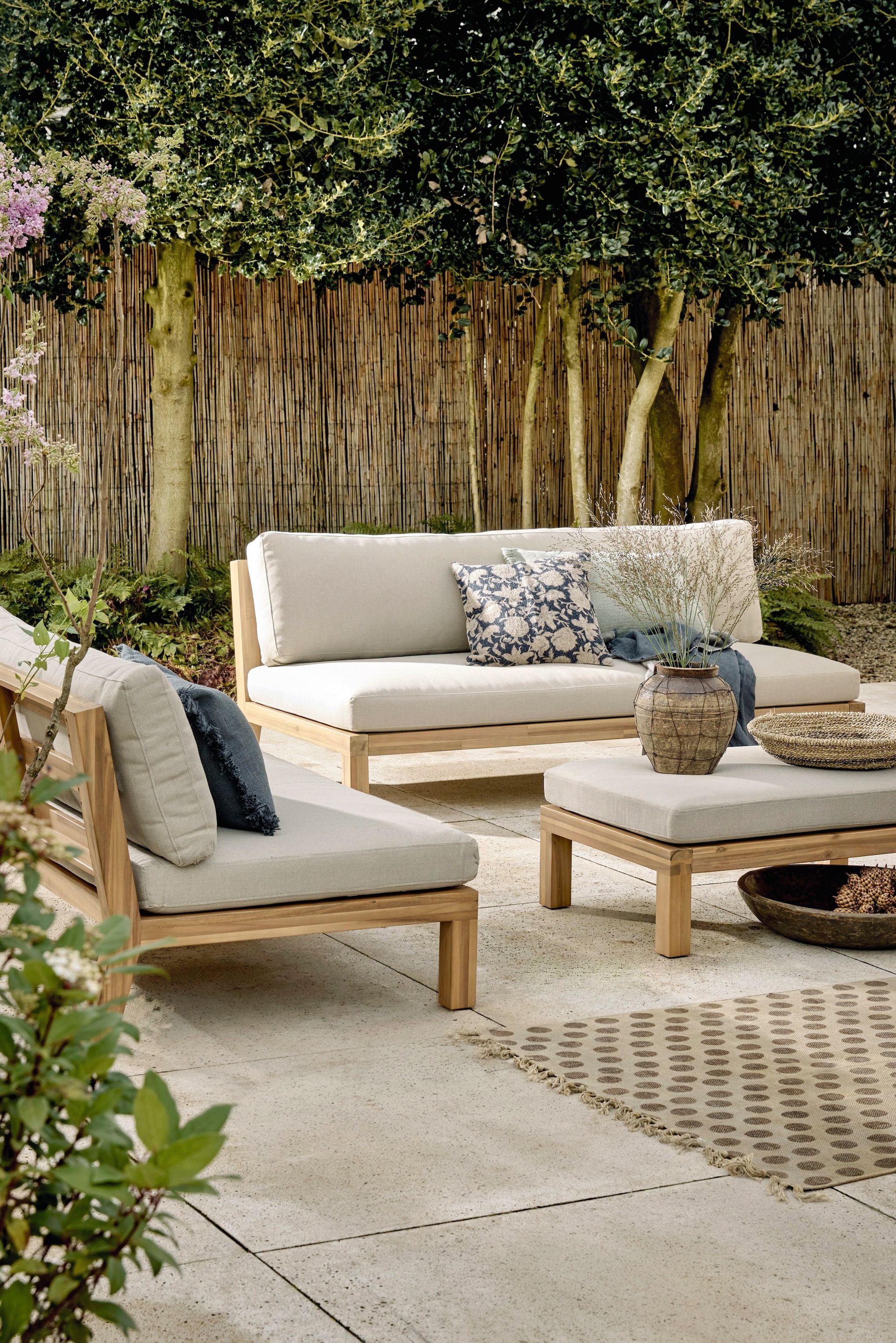 vtwonen tuinbank Relax, fsc-gecertificeerd acaciahout en stof, naturel en zand, 180x90x70 cm (bxdxh) € 749,-, vtwonen loungestoel Relax, fsc-gecertificeerd acaciahout en stof, naturel en zand, 120x70x90 cm (bxdxh) € 549,-, vtwonen hocker/bijzettafel Relax, fsc-gecertificeerd acaciahout en stof, naturel en zand, 90x60x40 cm (bxdxh) € 349,-M.m.v. zarahome.com (kussens, plaid en vaas), loods5.nl (mand, vloerkleed, grote houten schaal). vtwonen 04-2026 | styling Kim van Rossenberg | fotografie Peggy Janssen