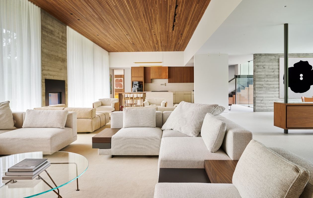 Witte bank Vincent Van Duysen voor Molteni & C. Beige bank Draga & Aurel voor Baxter. Fauteuils Living Divani. Glazen tafel vtintage. Op maat gemaakte walnoothouten keuken met travertijn eiland. Krukken van Antonio Citterio voor B&b Italia. Lampen Luceplan. Links naast keuken schilderij Jeroen Broux. vtwonen Design 03-2026 | fotografie Valentina Sommariva