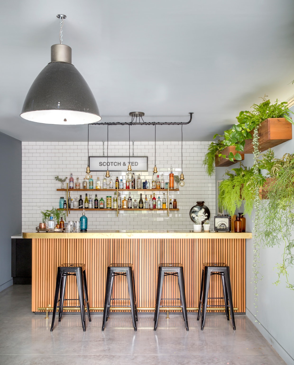 De cocktailbar in de kelder. Het bord aan de muur verwijst naar Sommers grootmoeder: ‘Ze had twee grote liefdes, mijn grootvader Ted en Scotch’. De bar is op maat gemaakt door Jason & Co. Aan de muur houten plantenbakken met veel hangende planten die de ruimte een natuurlijke uitstraling geven. vtwonen 01-2020 | fotografie Rei Moon / Living Inside