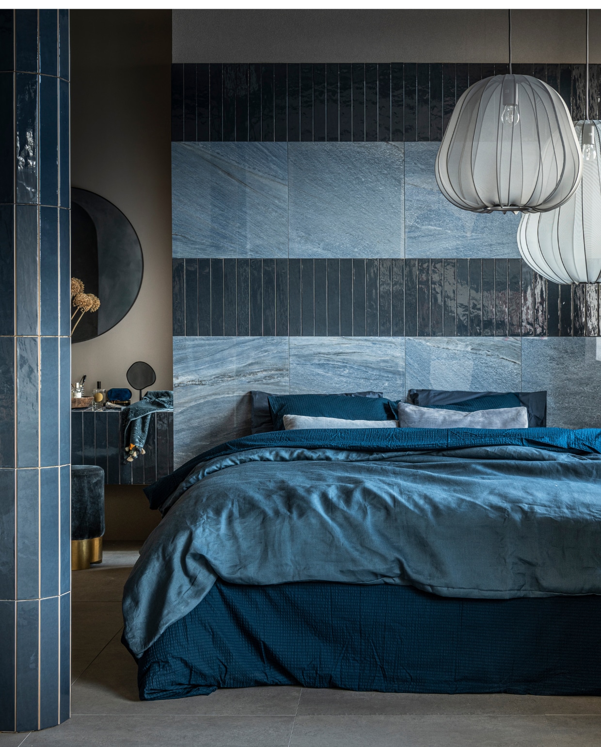 vtwonen collectie (Op de wand: vloer- en wandtegel Classic in kleur Heavenly Blue, glans, 60x60 cm, per m² € 77,95 (in mat € 71,90), wandtegel Marrakesh in kleur Ocean Blue, glans (ook in mat), 6,5x40 cm, per m² € 62,35. Op de vloer: vloertegel Raw in kleur Grey, 80x80 cm, per m² € 65,-). M.m.v. vtwonen.nl (stoffen hanglampen van Bolia), zarahome.com (ronde spiegel, staande spiegel, handdoek, donkerblauw beddengoed Minte van Essenza), ikea.nl (lichtblauw beddengoed Puderviva), melchiorinterieur.nl (poef, kussens), suhka.nl (houten schaal).