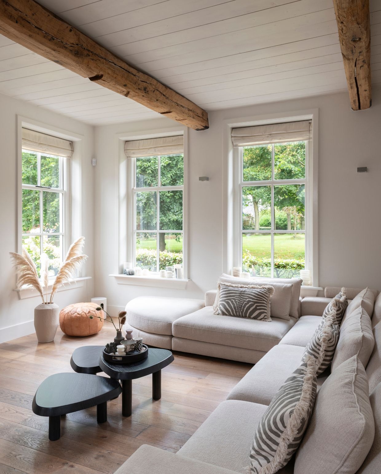 Modulebank en salontafels Eichholtz. Bruine leren poef uit Marokko, soortgelijke Houseify. Vaas en kussens H&M Home.