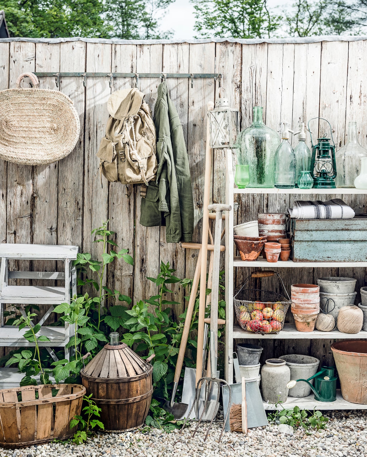 Trapje, stellingkast, fles in mand, rugzak, oude hark, groene vaas, glazen vaas, spuitflessen (Burbri Antiek). Kapstok, houten mand, oude lantaarn, kleine groene vaasjes, terracotta potten met bruin glazuur, witte bloempotten, grijze bloempot, grijze stenen vaas met ronde hals (De Weldaad). Rieten tas met leren details (Sukha Amsterdam). Jas, opgevouwen stof met blauwe streep (Six and Sons). Nieuw tuingereedschap, groene gieter (De Wiltfang). Handveger, veegblik (Loods 5). Groene lantaarn vanaf (Dille & Kamille). Terracotta bloempotten, oogstmand (Fleurmonde). Gereedschapskist (Brût Amsterdam). vtwonen special 01-2026 | fotografie Sjoerd Eickmans | styling Danielle Verheul