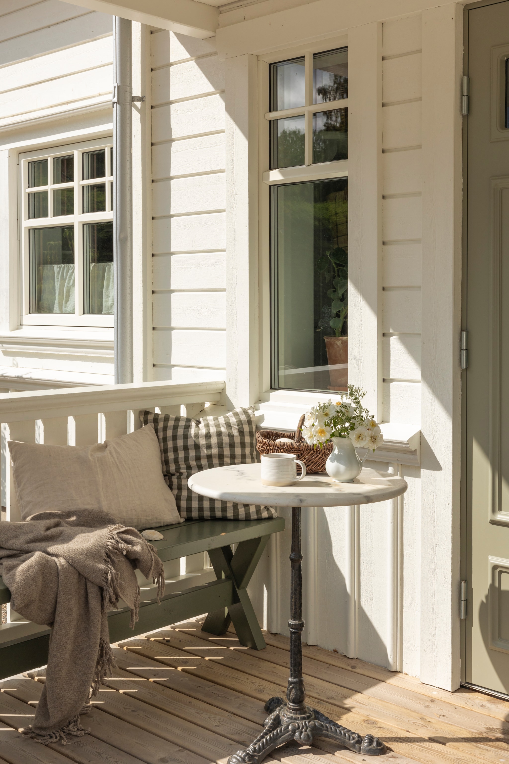Kleur houtwerk van het huis Utevit, kleur voordeur en bank in kleur Stensöta van Beckers. Voordeur Britta van Diplomat. Tafel, mand en vaas tweedehands. Rozen uit eigen tuin. vtwonen Landelijk 07-2026 | productie Sarah MacAfie | styling Anna Bjelkholm | fotografie Anna Karlsson