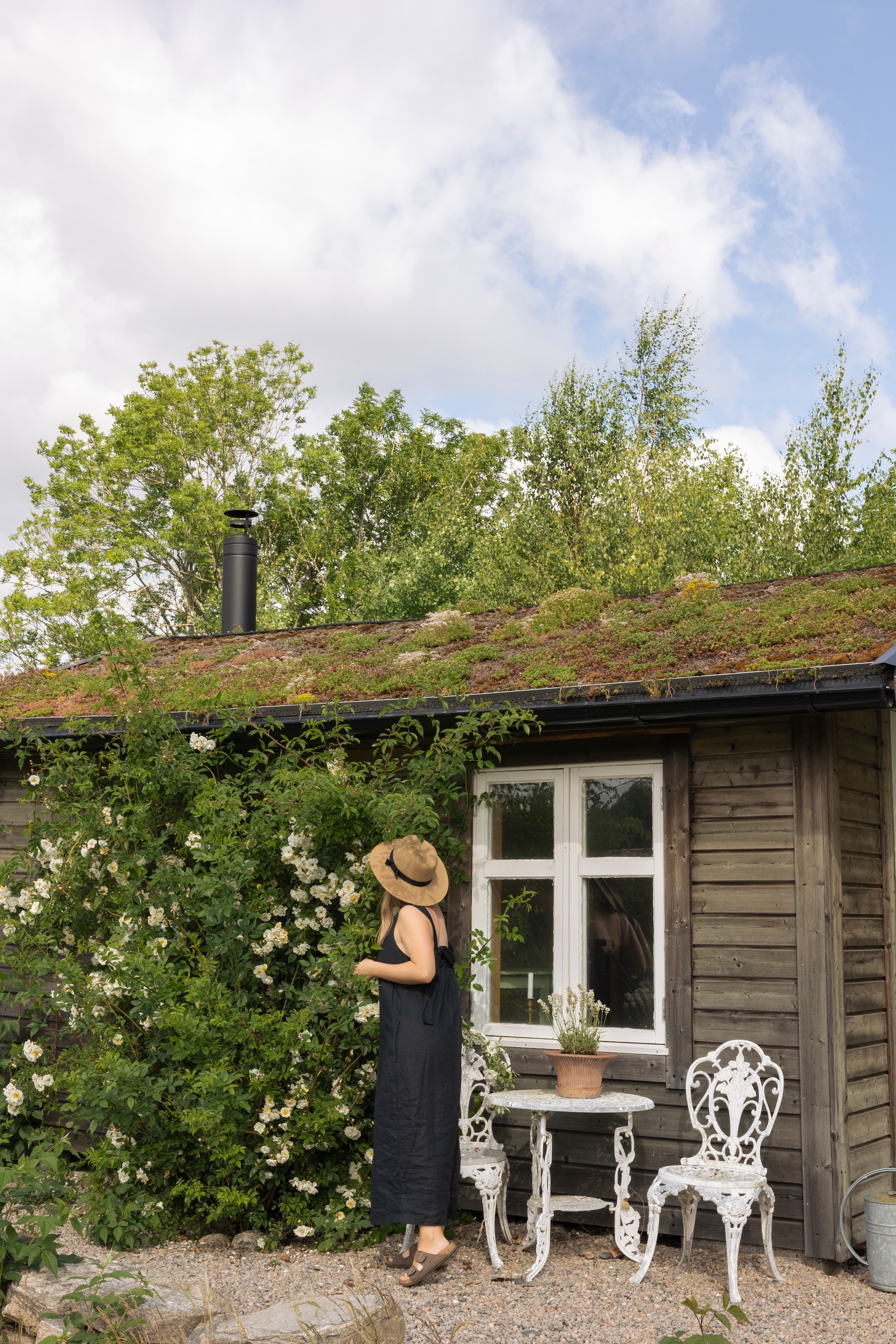 Saunahuisje met sedumdak. Ertegenaan groeit een ramblerroos. Gietijzeren tuinset vlooienmarkt. vtwonen Landelijk 07-2026 | productie Sarah MacAfie | styling Anna Bjelkholm | fotografie Anna Karlsson