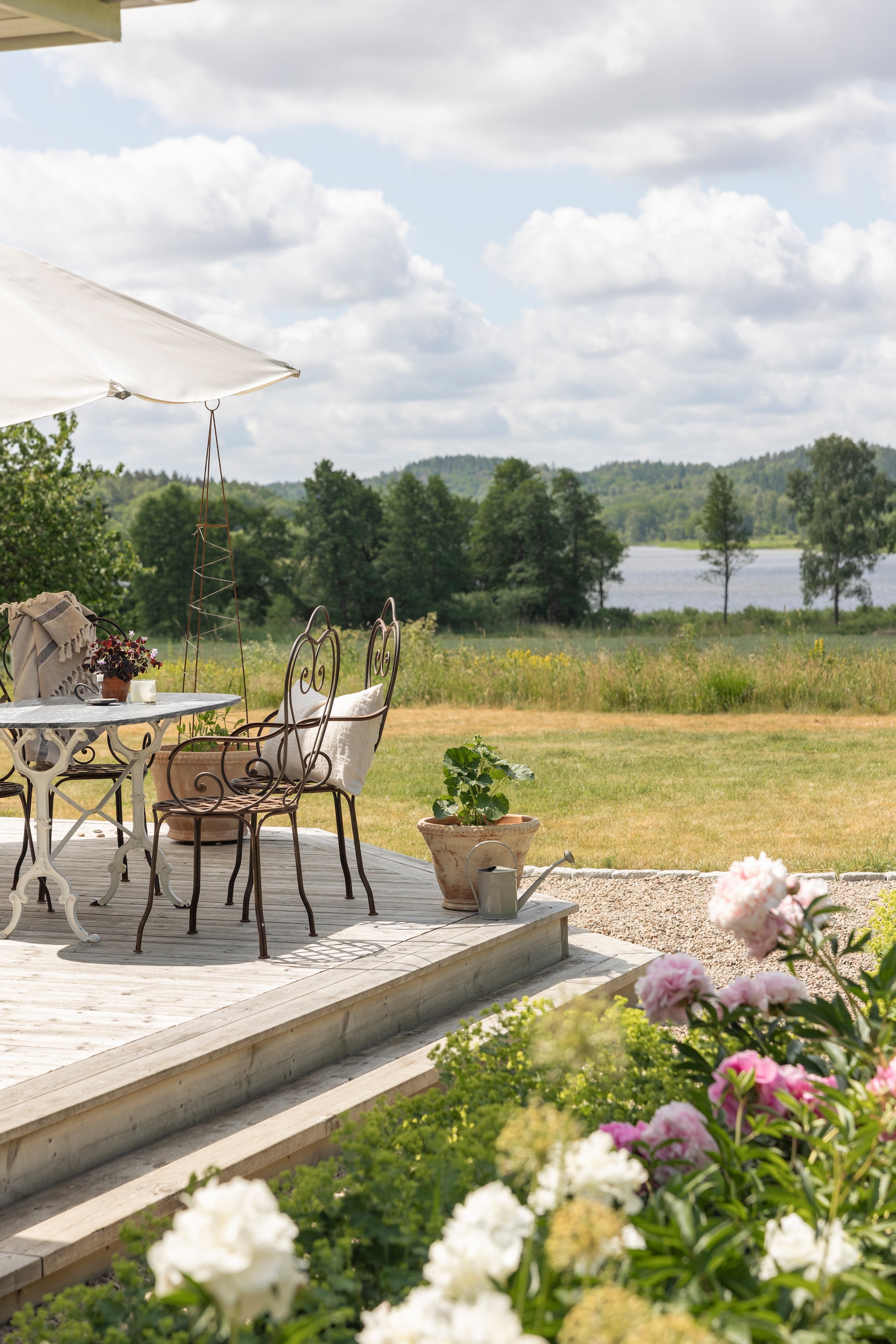 Tafel, stoel, bloempot en gieter tweedehands. Rondom het terras bloeien pioenrozen. vtwonen Landelijk 07-2026 | productie Sarah MacAfie | styling Anna Bjelkholm | fotografie Anna Karlsson