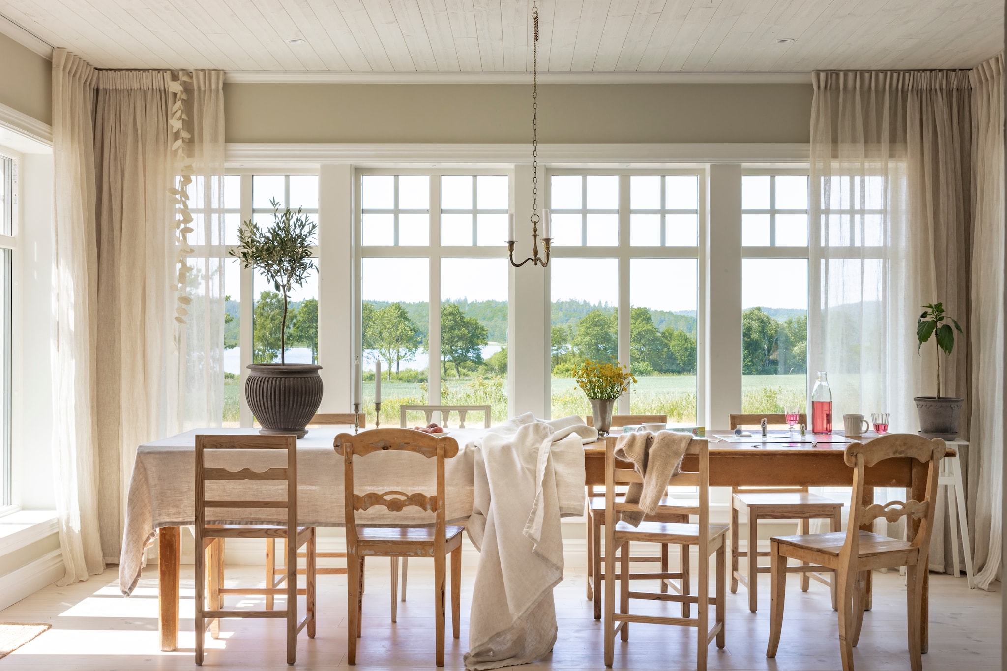 Ramen Elitfönster. Tweedehands houten tafel Antikkompaniet in Larv. Vurenhouten vloer afgewerkt met witte hardwaxolie. Stoelen tweedehands. Gordijnen en tafelkleed oud linnen. Accessoires kringloop. vtwonen Landelijk 07-2026 | productie Sarah MacAfie | styling Anna Bjelkholm | fotografie Anna Karlsson