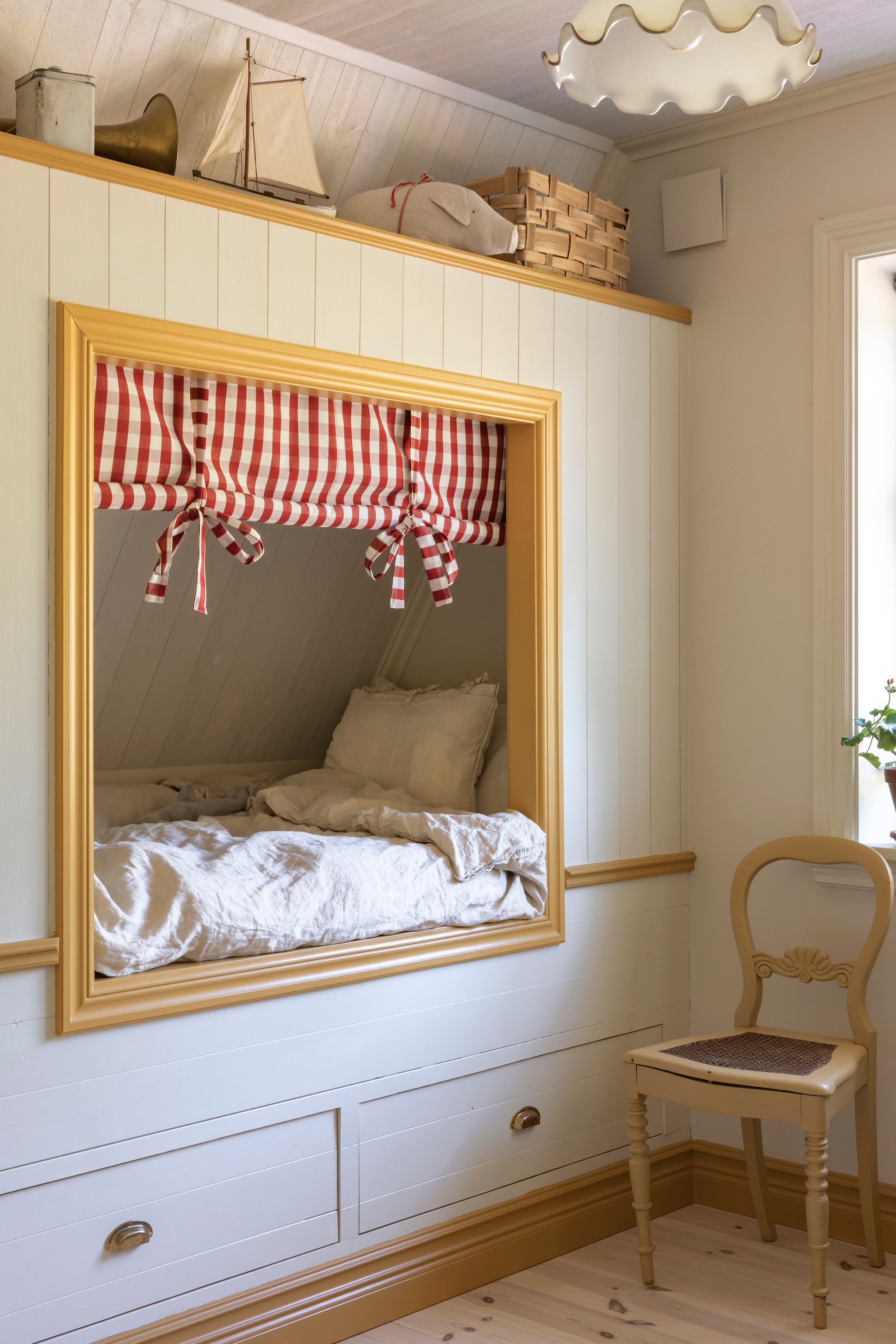 Ralphs bed met lades tot aan de muur bouwde Sarah zelf. Gordijn zelfgemaakt van stof Gripsholmsruta. Muren en bed geverfd met kleur Sans van Jotun, de omlijsting in kleur Masala van Jotun. vtwonen Landelijk 07-2026 | productie Sarah MacAfie | styling Anna Bjelkholm | fotografie Anna Karlsson