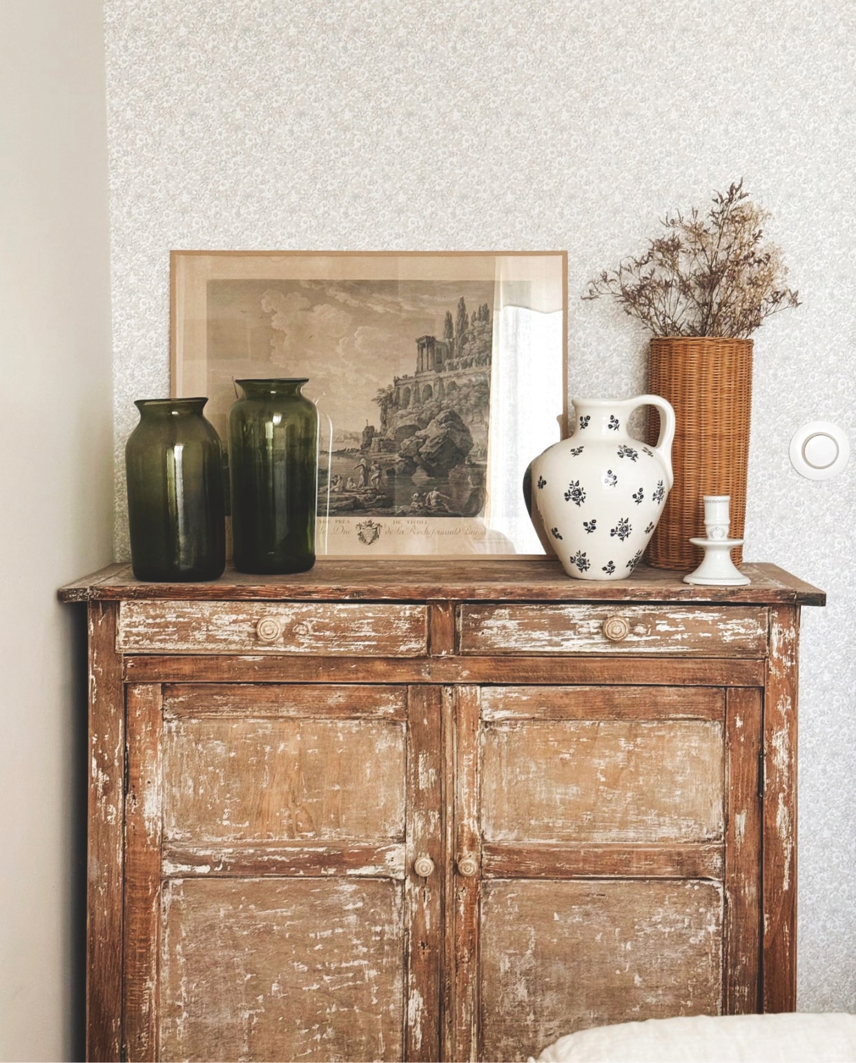 Parijse buffetkast van gepatineerd hout. Illustratie vintage. 19e-eeuwse geblazen glazen potten rommelmarkt. Rieten vaas met gedroogd limonium tweedehands. vtwonen Landelijk 04-2026 | fotografie Roxanne Dupoirier