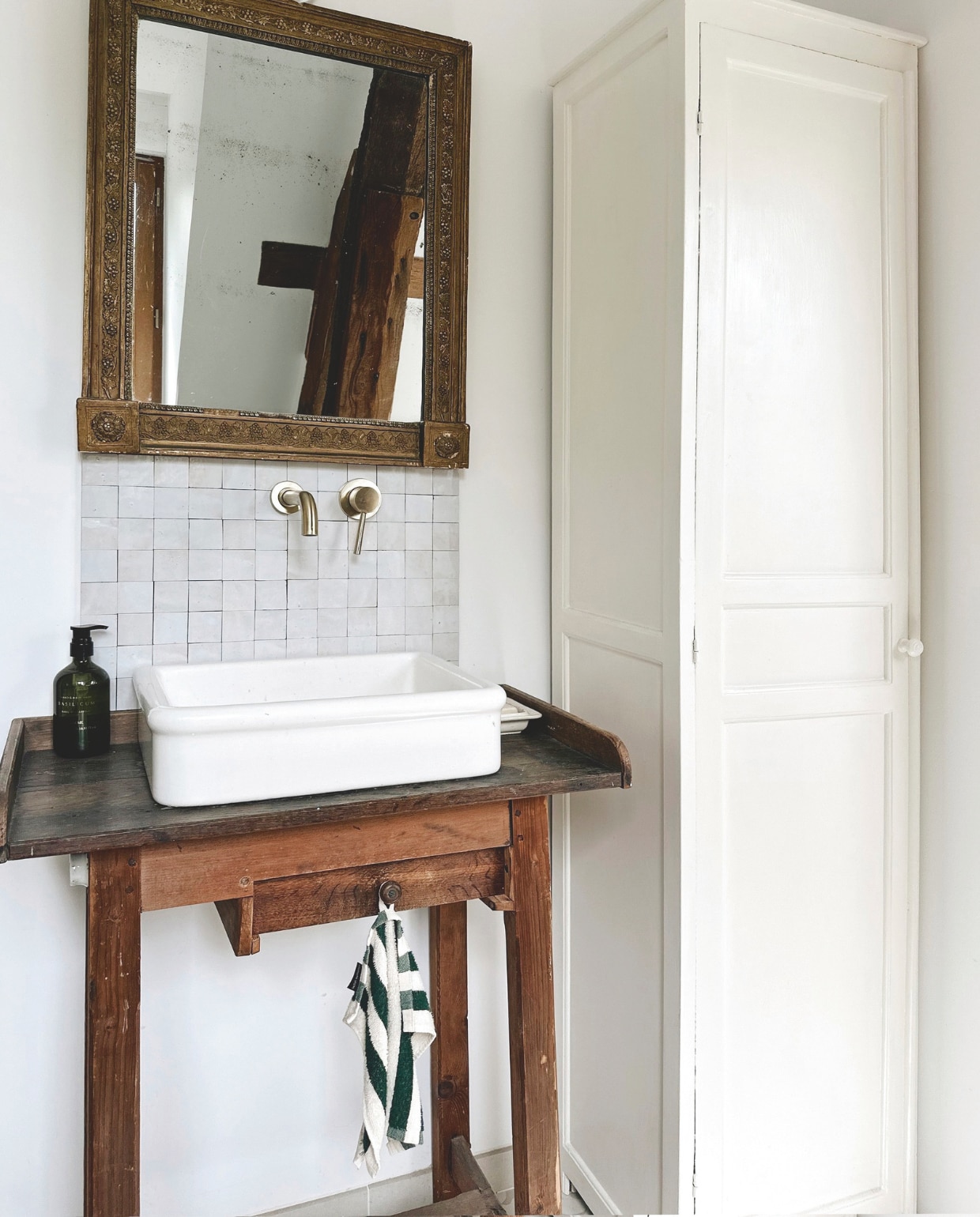 Kledingkast gevonden op Les Puces du Canal. Spiegel met verguld kwik en druiventrosmotief, werkbank en porseleinen gootsteen vintage. vtwonen Landelijk 04-2026 | fotografie Roxanne Dupoirier