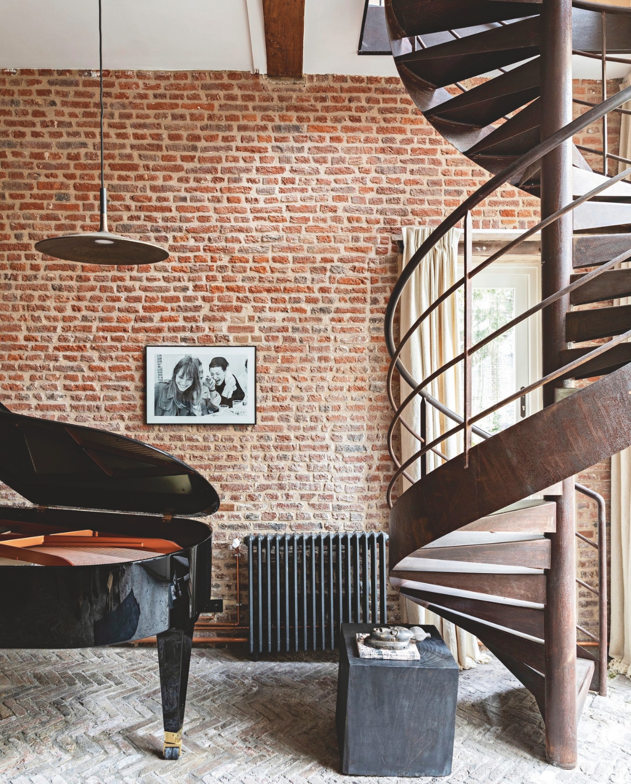 Kantoor en muziekkamer in de voormalige 18e-eeuwse stal. Bakstenen vloeren en muren origineel. Wenteltrap dateert van de vorige renovatie. Vintage gietijzeren radiator gerestaureerd door Gilentik. Hanglamp Frezoli Lighting. Kastje Pachulí Interior. Afrikaans masker meegebracht van een reis. Ingelijste foto cadeau van vrienden. Vleugel Bösendorfer. vtwonen Landelijk 04-2026 | styling Marie-Maud Levron | fotografie Yann Deret