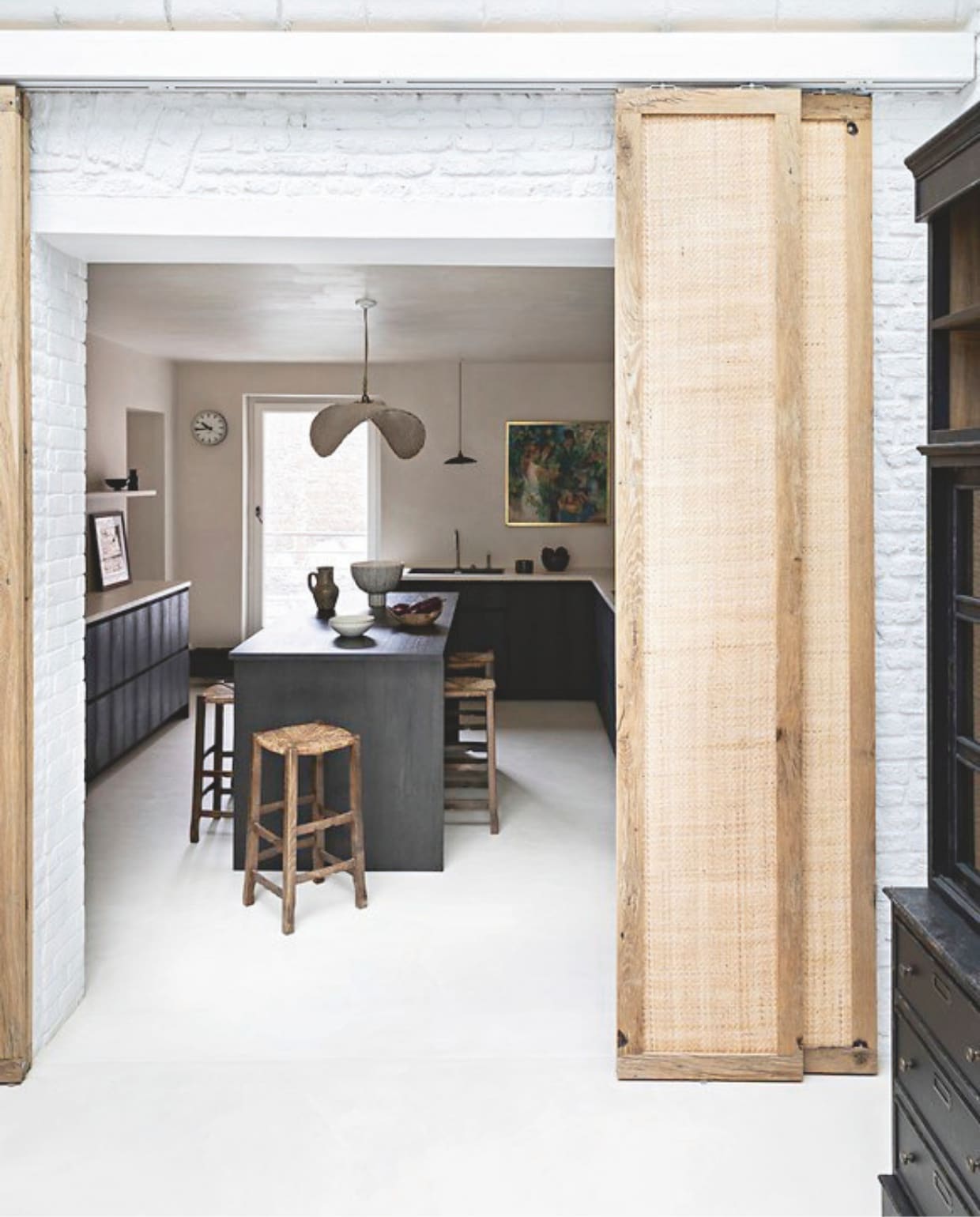 Maatwerk keuken van zwart gebeitst verouderd eikenhout van Atmosphère Bois. Werkbladen, muren, plafond en vloer van gepolijst beton in Parchemin door Marius Aurenti. Schilderij erfstuk. Klok Selency. vtwonen Landelijk 04-2026 | styling Marie-Maud Levron | fotografie Yann Deret