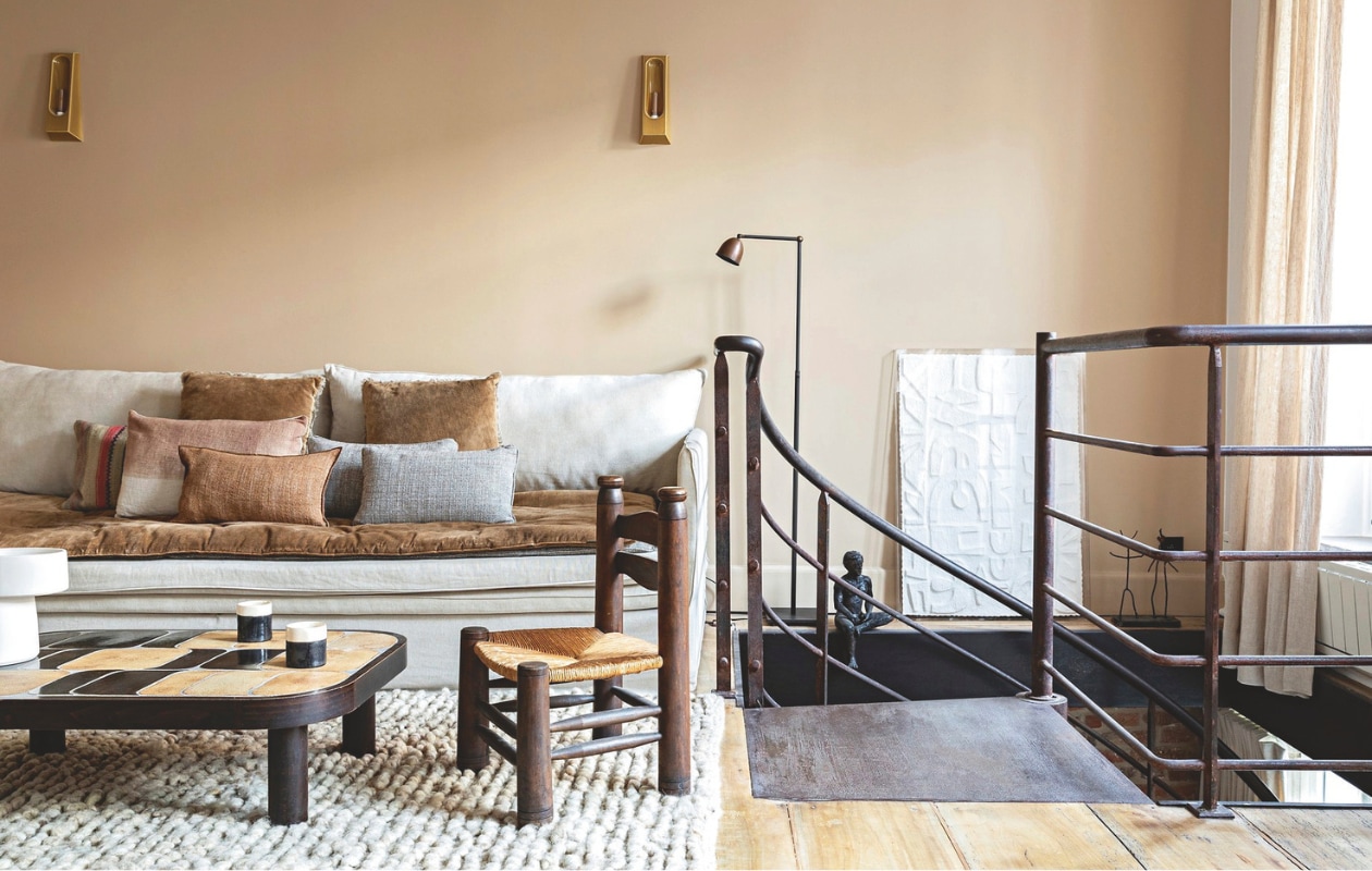 Woonkamer op eerste verdieping. Muurverf Florence van Ressource. Gordijnen Fior di latte en terracotta kussens van Maison de Vacances, gemaakt door William Brouillard. Wand-lampen Alcove van Violaine d’Harcourt. Staande lamp Frezoli Lighting. Vloerkleed Luca van Nunamae. Bank, rugkussens en grijze kussens Berengere Leroy. Tie-dye kussen Bed and Philosophy. Salontafel van vlooienmarkt van Saint-Ouen. Sculptuur vondst van de bewoners. Schilderij Am.pm. Kopjes gemaakt door de bewoners. Vintage stoel Désuet. vtwonen Landelijk 04-2026 | styling Marie-Maud Levron | fotografie Yann Deret