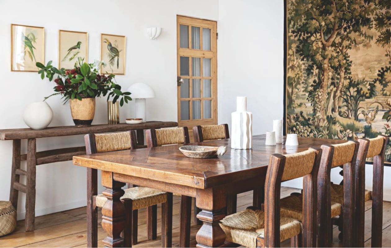 Privé-eethoek. Muurverf kleur L’Innocent van Ressource. Eettafel en houten vaas vlooienmarkt van Saint-Ouen. Stoelen, hanglamp en houten bord Selency. Grote witte vaas Am.pm. Set van drie kleine vazen Epure Céramique. Wandtafel Atmosphère d’Ailleurs. Tafellamp Le Redoute. Gouden vaas en schaaltje H&m Home. Vogelschilderijen erfstukken. Wandlamp Alix D. Reynis. vtwonen Landelijk 04-2026 | styling Marie-Maud Levron | fotografie Yann Deret