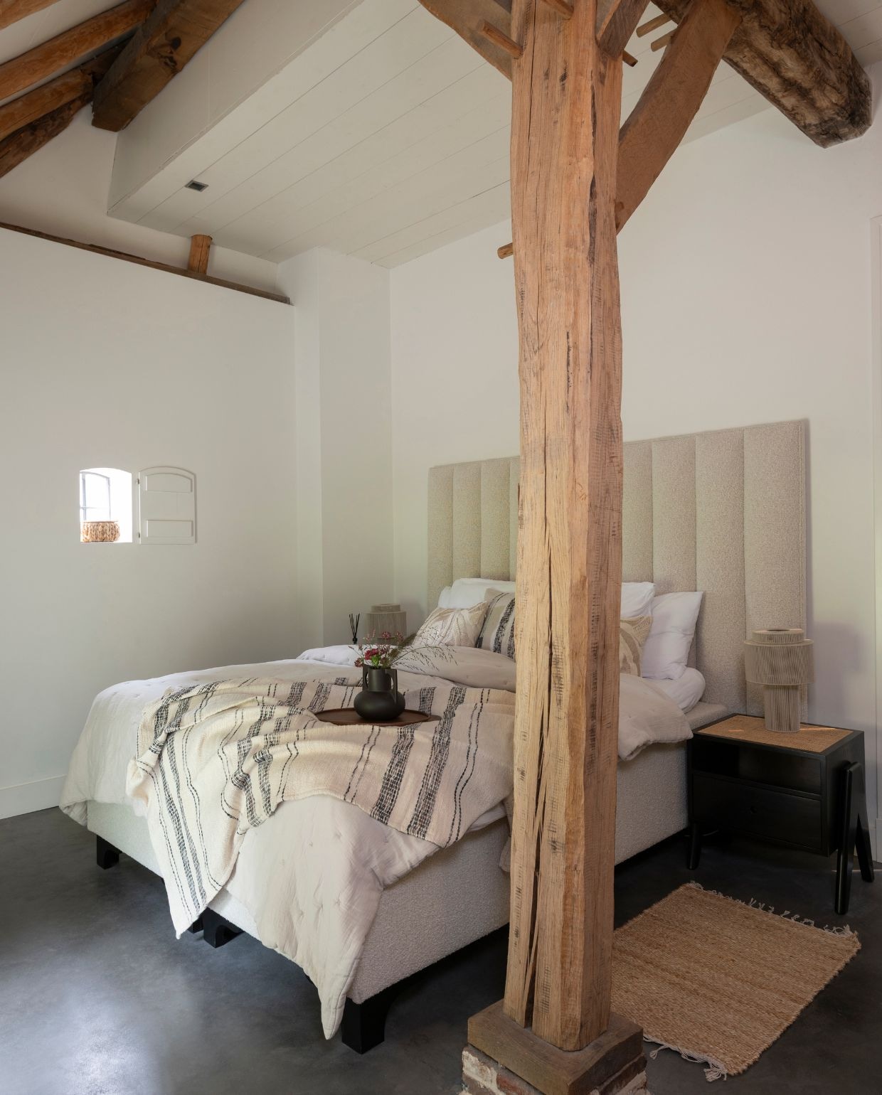 Badmat Aquanova. Boxspring en stoel Eichholtz. Lampen, kussens, plaid en dienblad Nordal. Vaas op dienblad H&m Home. Soortgelijke gevlinderde betonvloer Willem Designvloeren. vtwonen Landelijk 03-2026 | fotografie Suzanne Paap