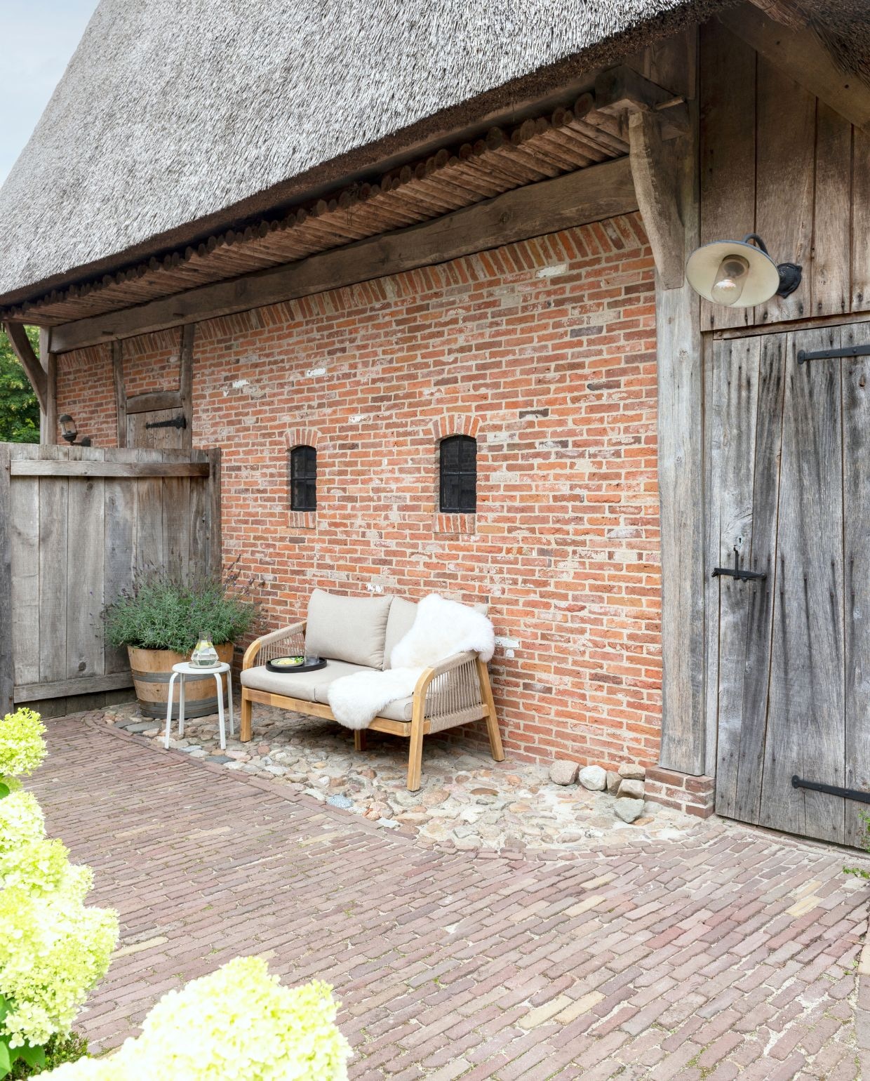 Als de zon schijnt, maar het nog fris is vanwege de wind, is de bank bij de schutting, uit de wind, favoriet. vtwonen Landelijk 03-2026 | fotografie Suzanne Paap