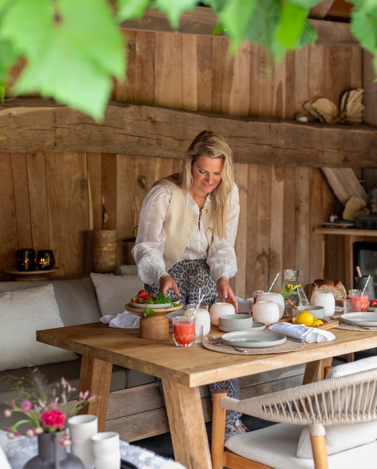 Judith zet alles klaar voor de lunch met het gezin. De overkapping is gemaakt van eikenhout, wat perfect aansluit bij de landelijke omgeving van de woonboerderij. vtwonen Landelijk 03-2026 | fotografie Suzanne Paap
