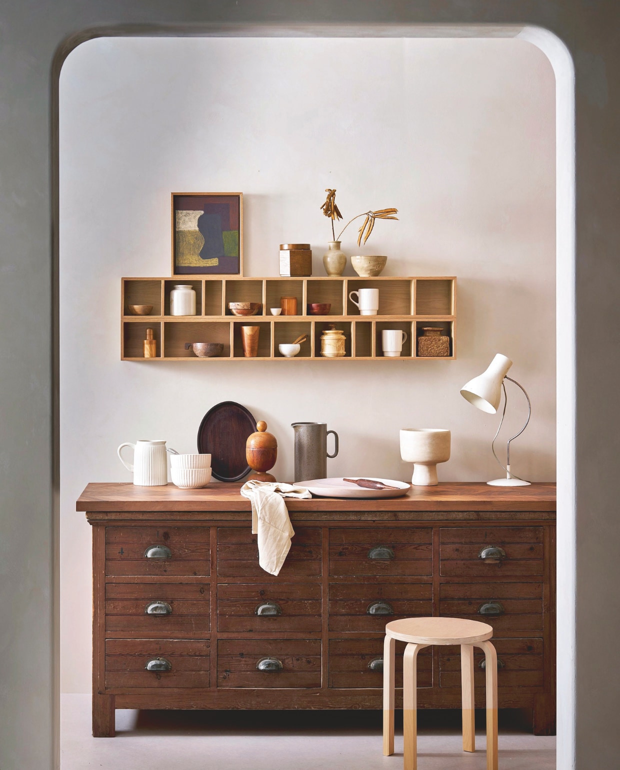 vtwonen wandkast Show it, mdf met fineer, naturel, 130x16x12 cm (lxbxd) € 89,95 (shop.vtwonen.nl).M.m.v. burbriantiek.nl (ladekast, lamp), edithbeurskens.com (schilderij), ikea.com (kruk), householdhardware.nl (schaal op voet), zarahome.com (ovaal dienblad), shop.vtwonen.nl (bekers, geribbelde kan, geribbelde kommen). Overig privébezit. vtwonen 04-2026 | styling Cleo Scheulderman | fotografie Jeroen van der Spek