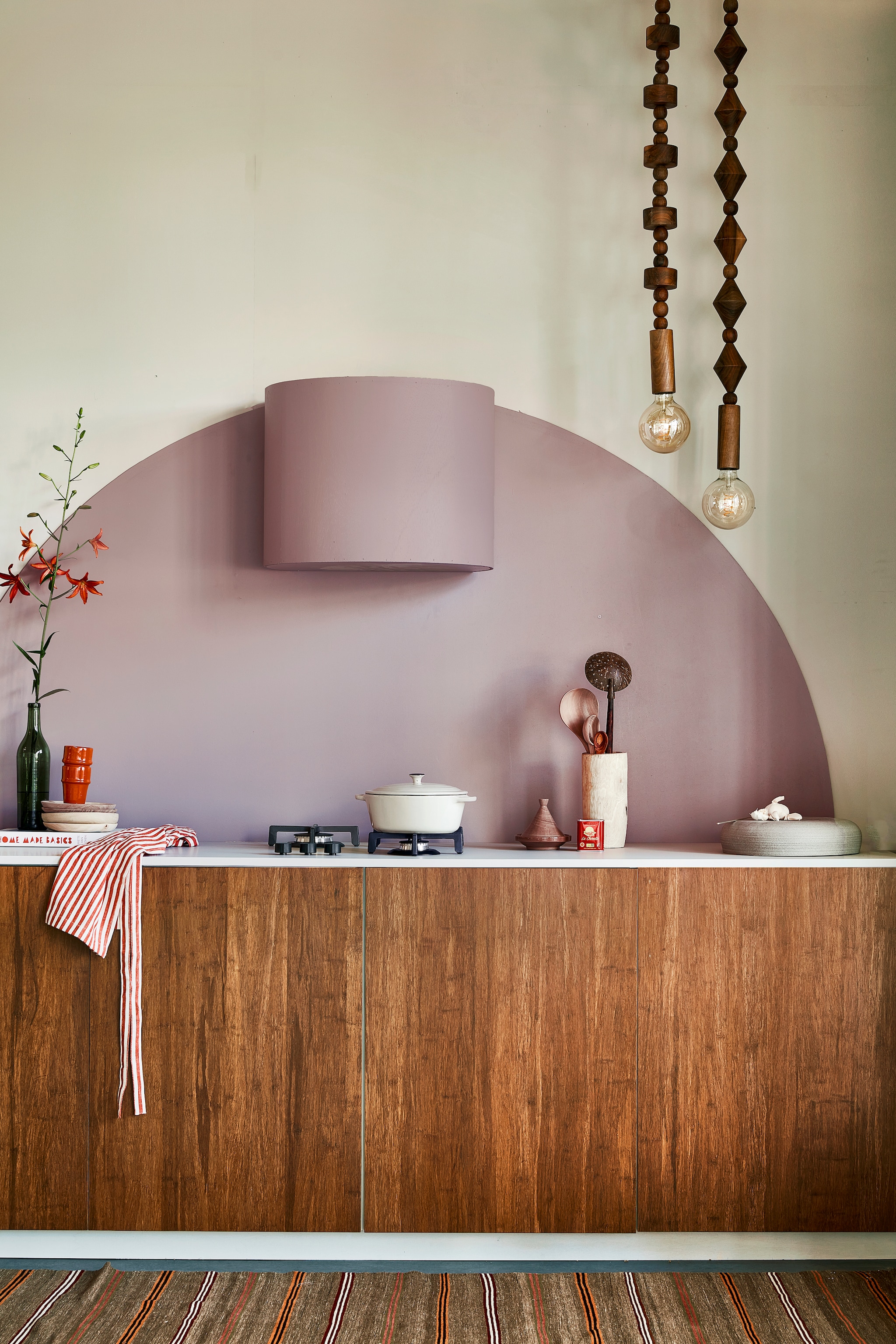 Muurverf Flexa Easycare Keuken kleur Cosmic Glory, ronde vorm en bekleding afzuigkap kleur Heart Wood, per liter € 25,49 (flexa.nl). Bamboe fronten Destiny Caramel, 60x80 cm (bxh) € 259,-, aanrechtblad prijs op aanvraag (frontz.nl). Vloerkleed vintage, 215x86 cm € 350,- (rozenkelim.nl). Groene fles € 7,50 (kringloop). Kookboek Home Made Basics van Yvette van Boven € 34,99 (bol.com). Kralenlampen, per stuk € 659,-, rode mokken € 9,95, houten borden € 21,-, pollepels vanaf € 9,95, houten vijzel € 36,-, kleine tajine € 8,50 (householdhardware.nl). Schort € 9,99 (hm.com). Aardewerken pan € 39,99 (zarahome.com). Handgemaakte turnaround dish € 185,- (lilokeramiek.nl). vtwonen 09-2022 | styling Leonie Mooren | fotografie Peggy Janssen