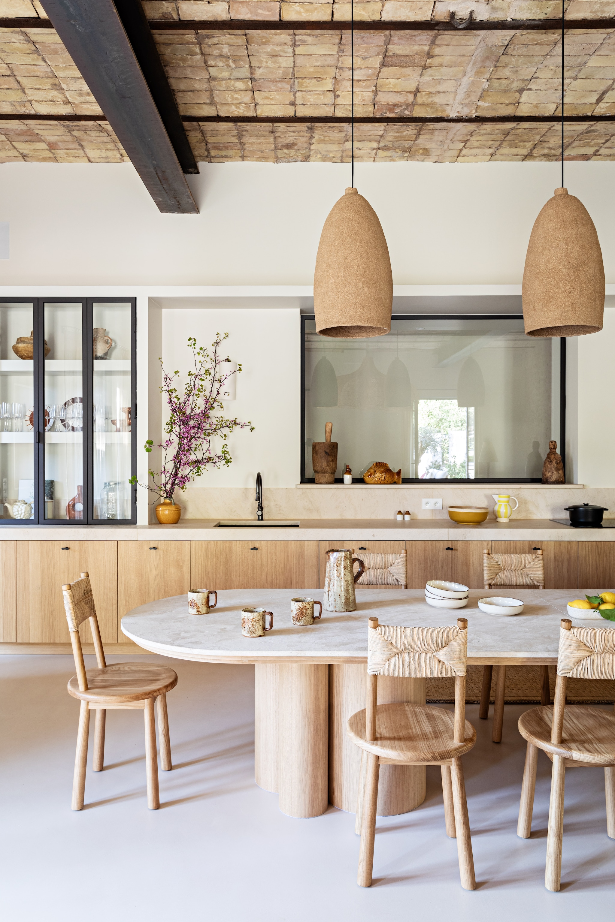Eiken keuken en eettafel maatwerk, werkblad en tafelblad crema bella-marmer. Hanglampen Zbozhzha. Stoelen La Chaiserie Landaise. Servies vintage en Carrefour. Vaas met takken Kave Home. vtwonen 08-2026 | styling Marie-Maud Levron | fotografie Yann Deret