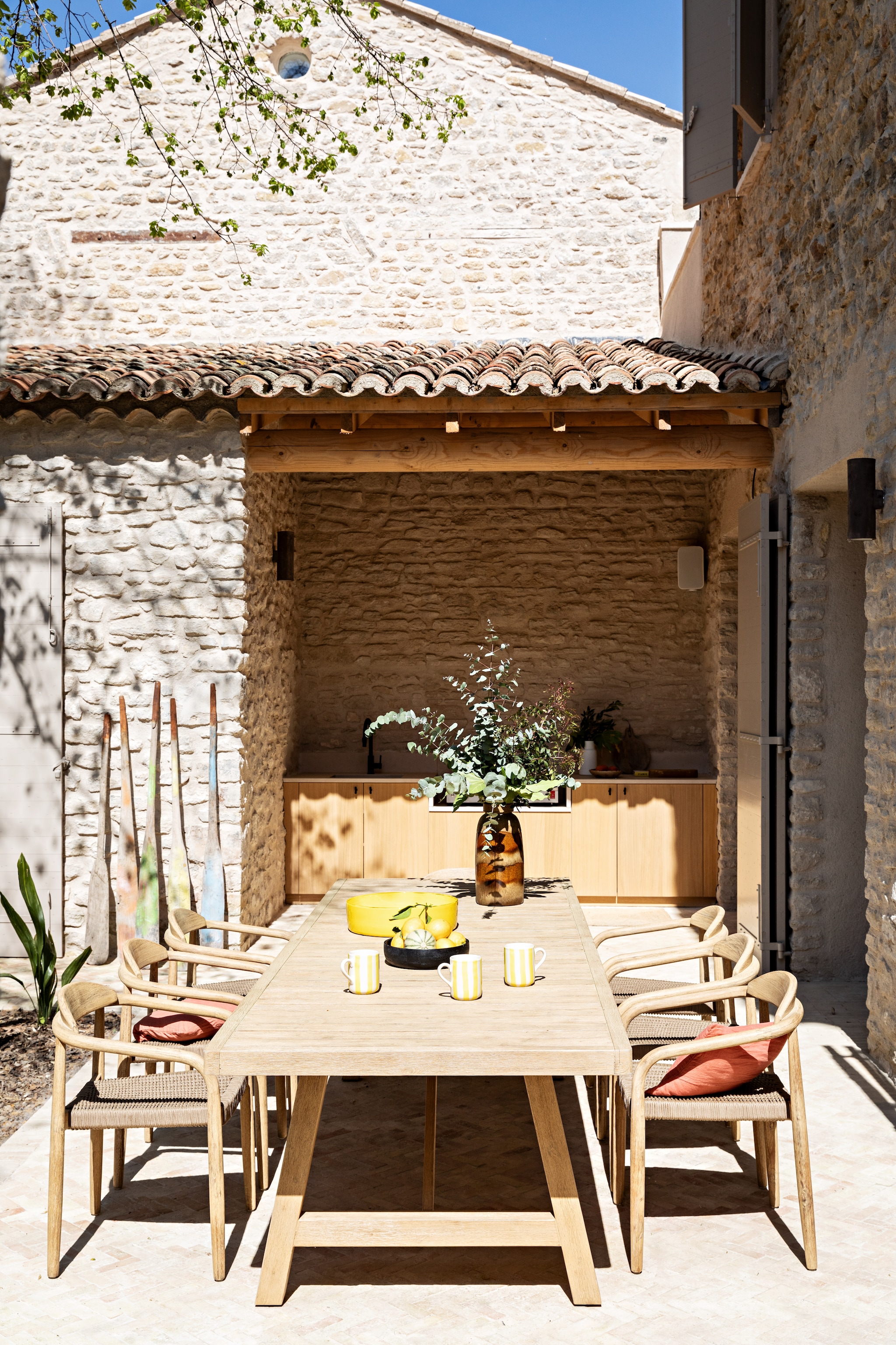 Tuintafel en stoelen Sklum. Vergelijkbare mokken vtwonen via shop.vtwonen.nl. Roeispanen vintage. Buitenkeuken maatwerk. vtwonen 08-2026 | styling Marie-Maud Levron | fotografie Yann Deret