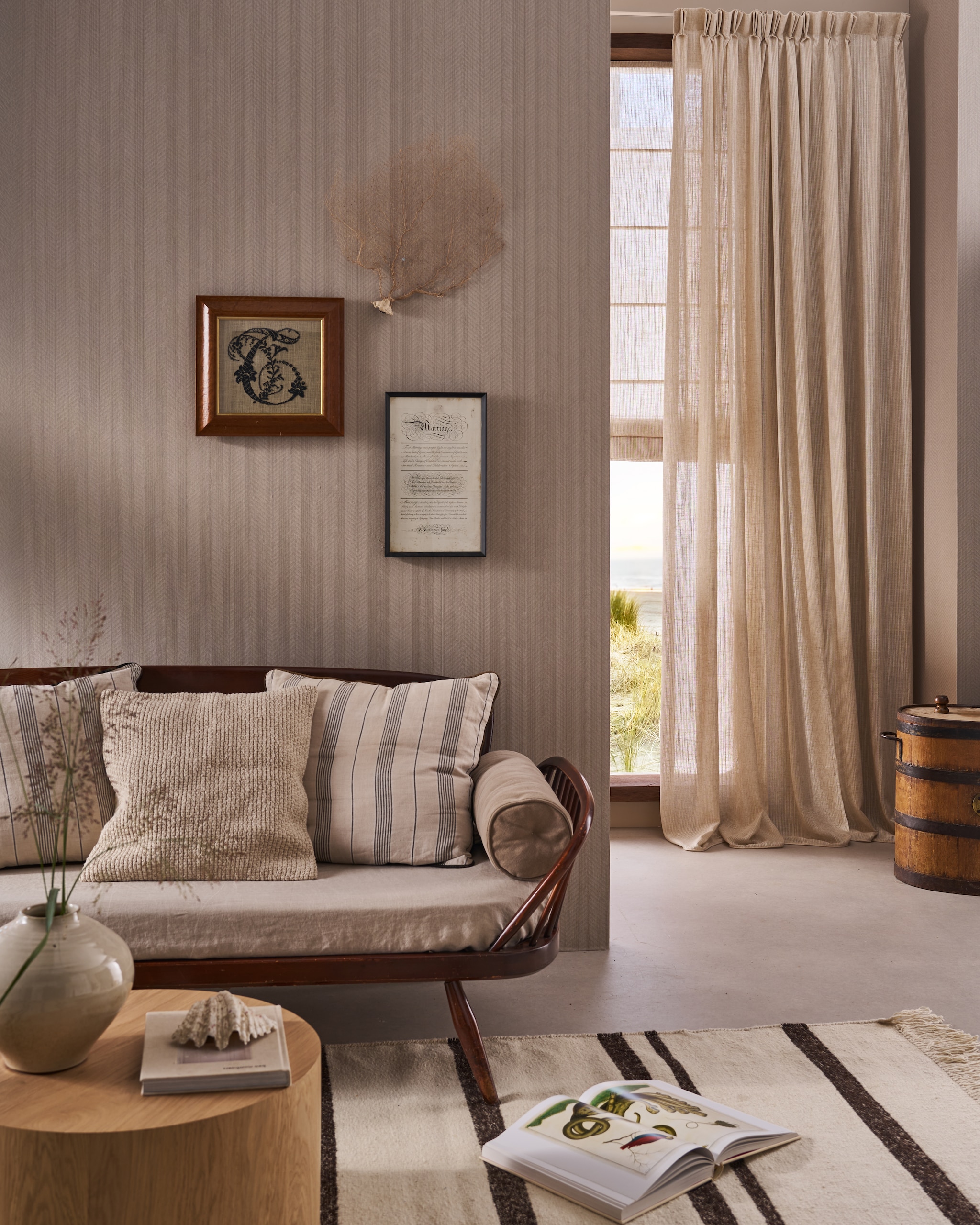 vtwonen behang Herringbone, vliesbehangpapier, soft naturel, 10 m x 53 cm (lxb), per rol € 35,99.M.m.v. hkliving.com (vloerkleed), pietjonker.nl (vintage bank), zarahome.com (vaas, naturel kussen en rolkussen), zuiver.com (eikenhouten salontafel), karwei.nl (gordijn, vouwgordijn en muurverf van vtwonen). Overig privébezit. vtwonen Landelijk 06-2026 | styling Cleo Scheulderman | fotografie Jeroen van der Spek