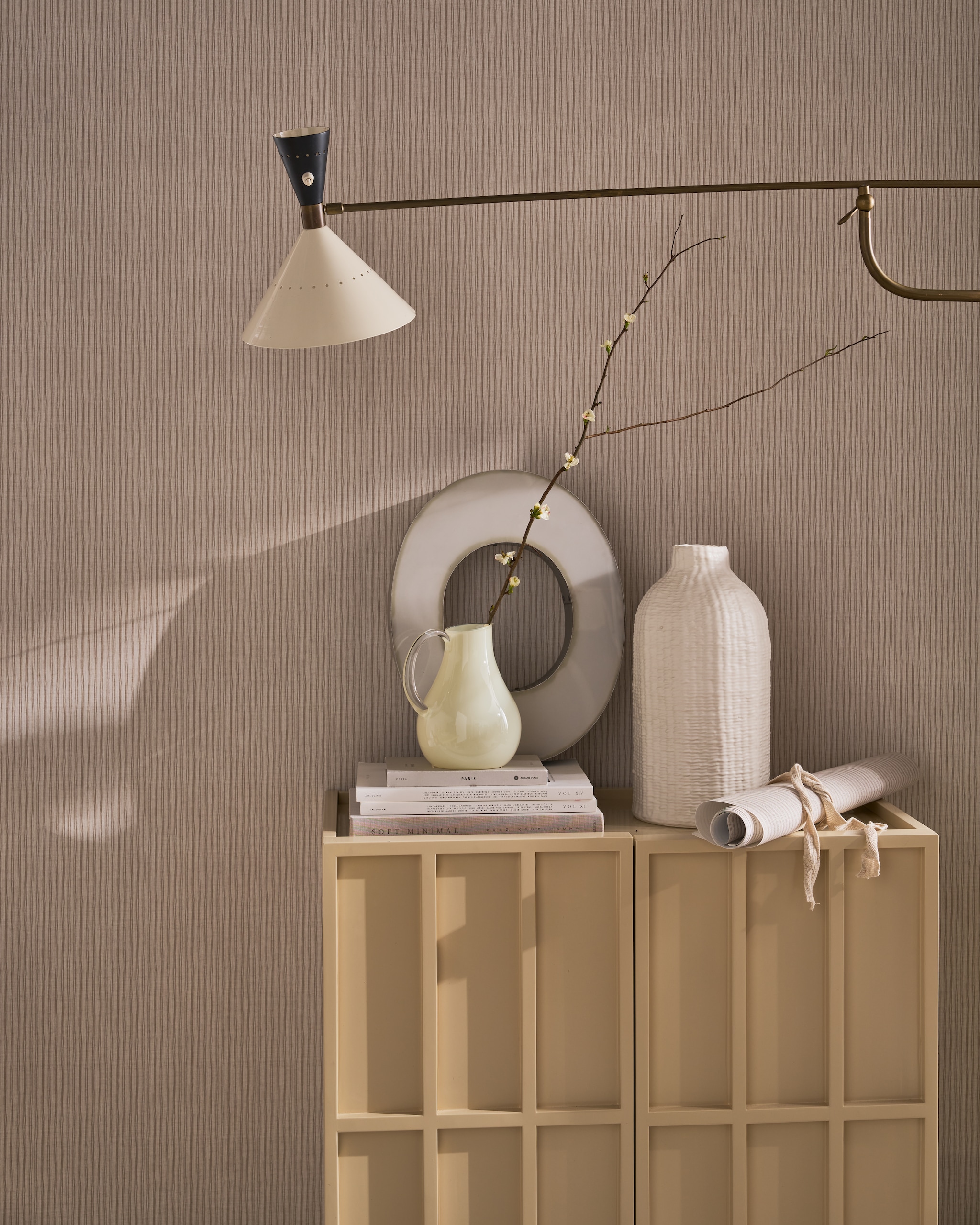 vtwonen behang op rol Double Stripes, vliesbehangpapier, warm grey, 53 cm x 10 m (bxl), per rol € 35,99.M.m.v. hkliving.com (dressoir). urbannatureculture.com (vazen), pietjonker.nl (wandlamp). Overig privébezit. vtwonen 07-2026 | styling Cleo Scheulderman | fotografie Jeroen van der Spek