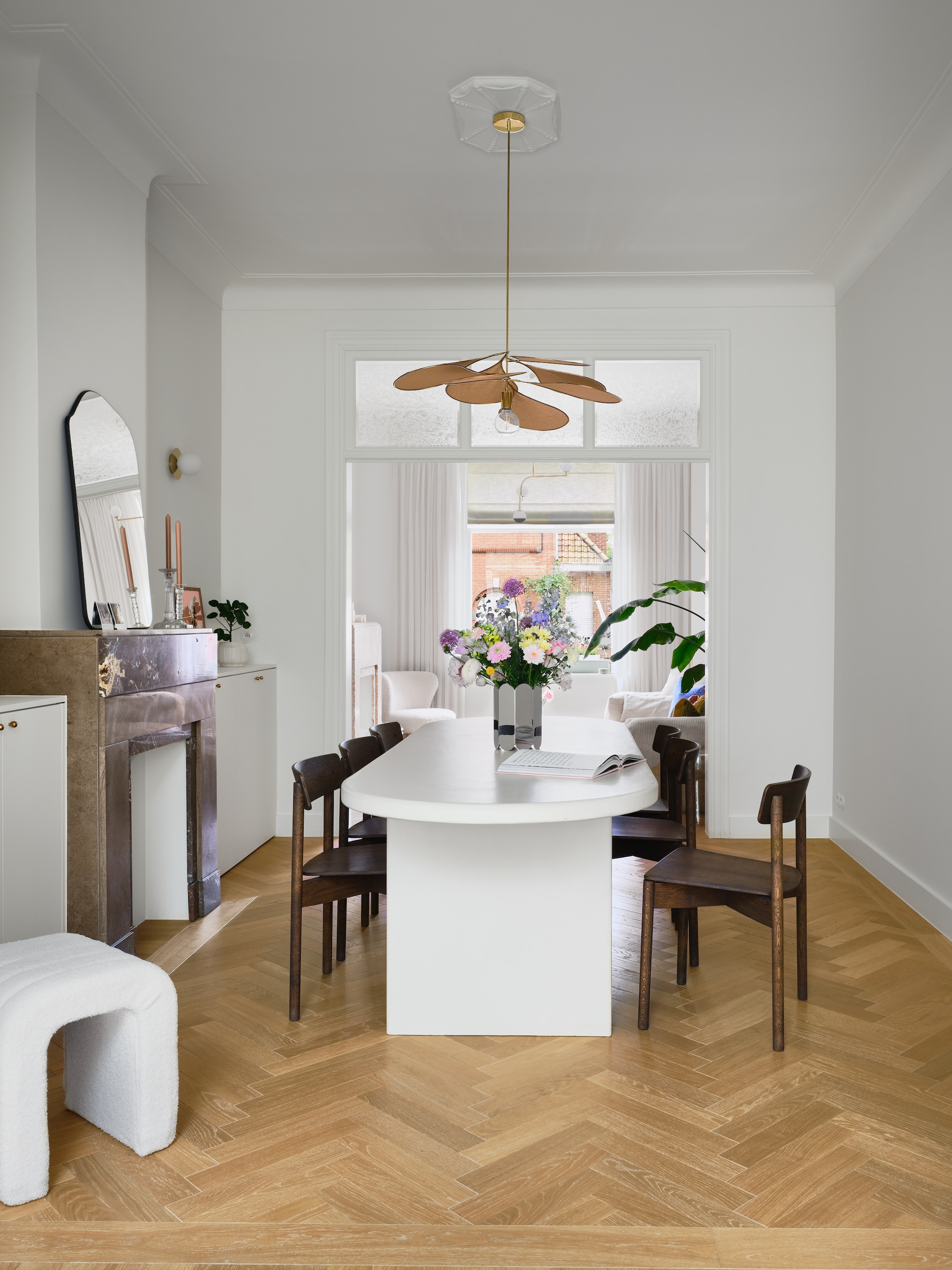 Wandkasten maatwerk naar eigen ontwerp. Messing kastgreepjes en deurklinken Dauby. Poef Kwantum. Tafel maatwerk, afgewerkt met microtopping van B.a.i.t. Stoelen Takt. Hanglamp Georges. Wandlampen H&m Home. Vaas spiegelglas Muller Van Severen voor Hay. Spiegel Zara Home. Vintage kandelaars. Waterfles Paveau. Eiken visgraat parket Avance in Valetta via Hout Luyten. vtwonen 07-2026 | fotografie Mr. Frank