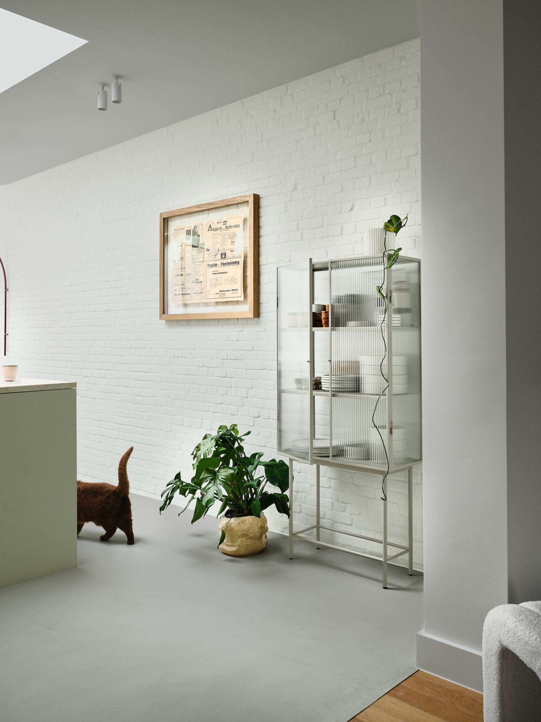 Glazen kast Ferm Living. Servies Salt & Pepper en HKliving. Ingelijst oud krantenartikel dat het stel vond bij de renovatie. Vloer Socrete in kleur 37 Early Cotto van Liquidfloors. vtwonen 07-2026 | fotografie Mr. Frank